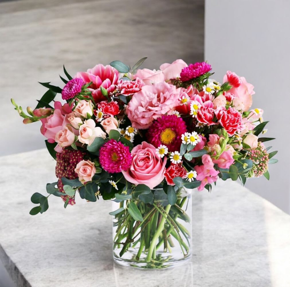 Rounded arrangement of pink roses, carnations, and mixed blooms in a clear glass vase