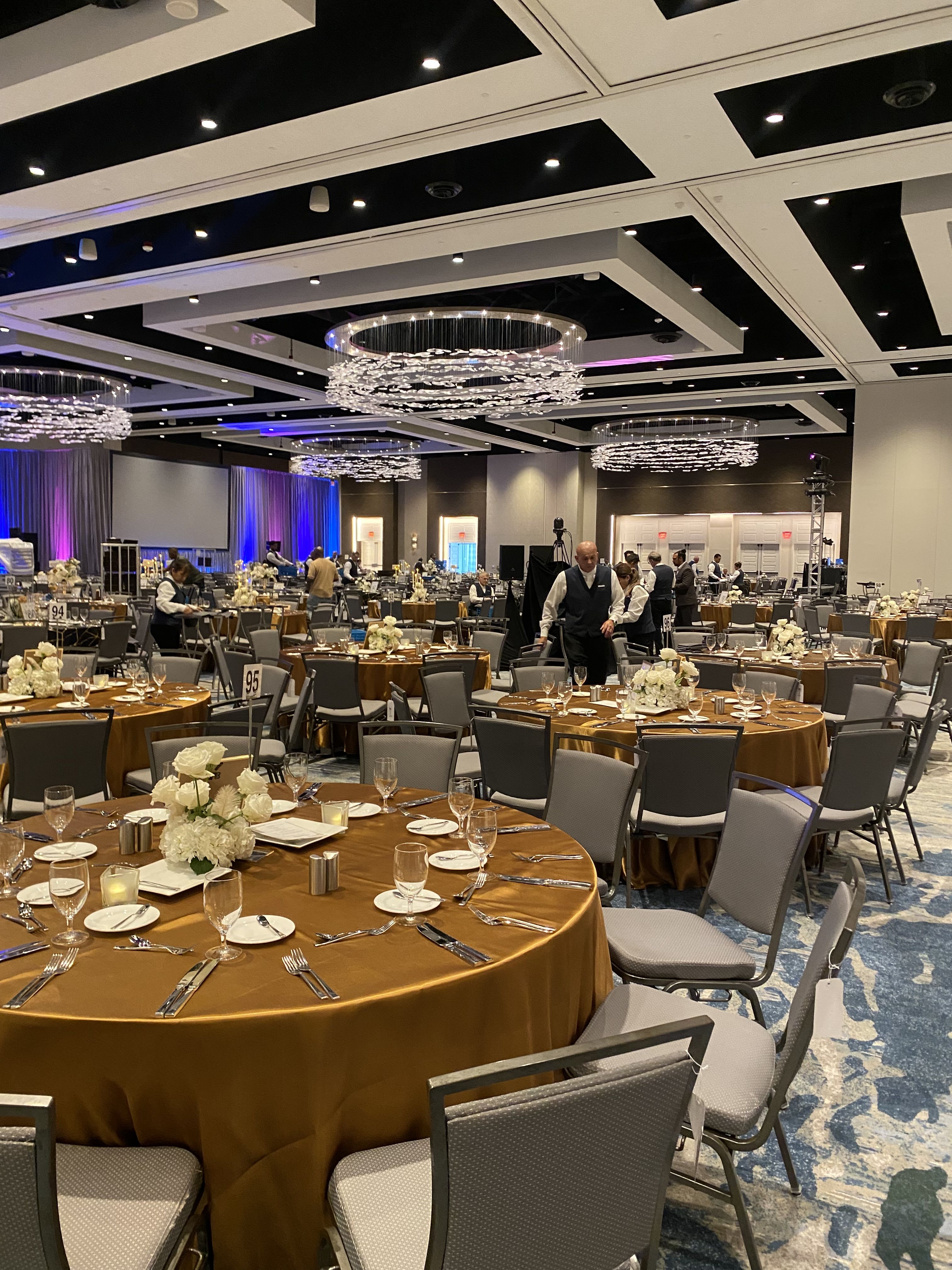 Large banquet hall with round tables and low white floral centerpieces.