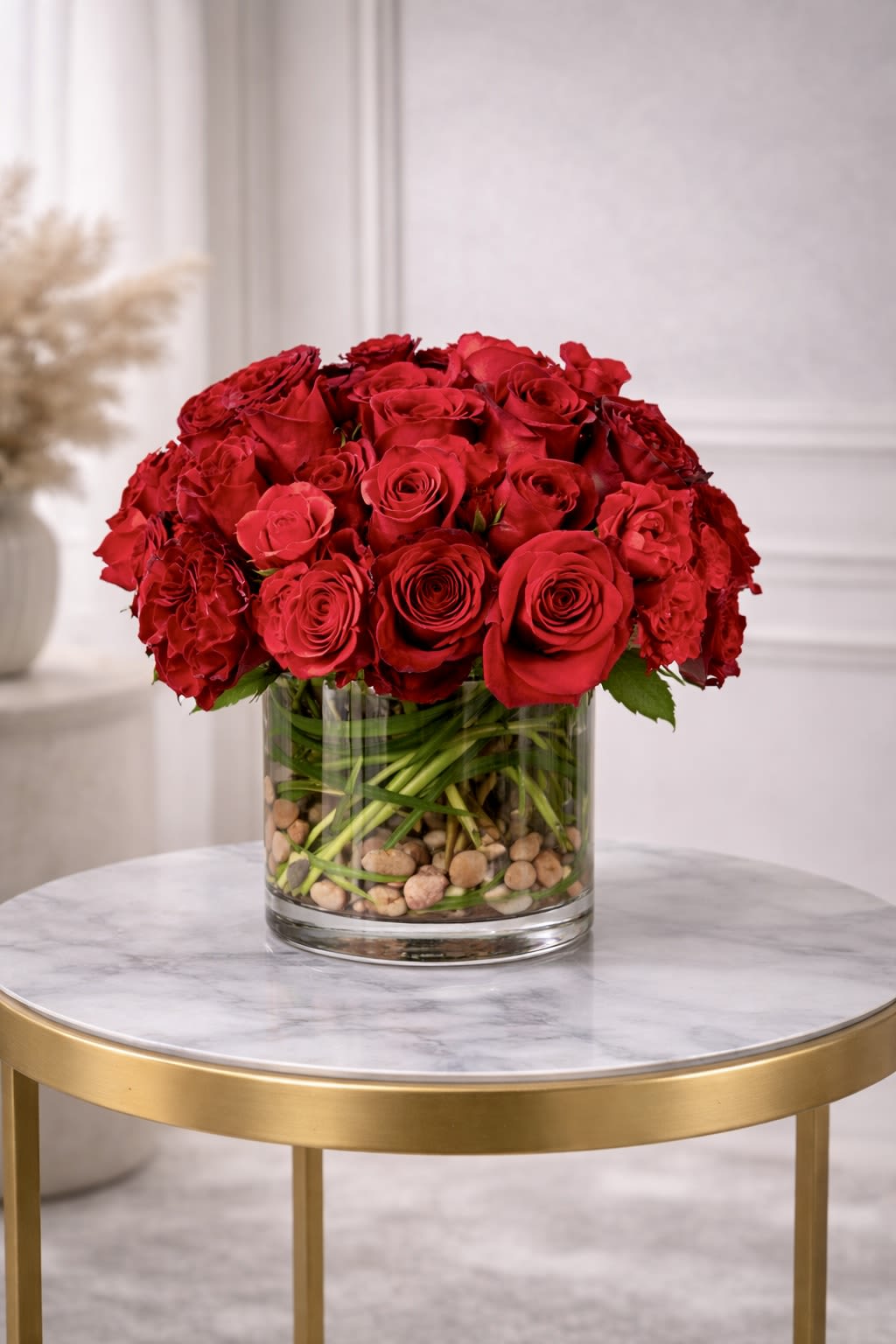 Low arrangement of red roses in a clear glass cylinder vase with stones on a small round table