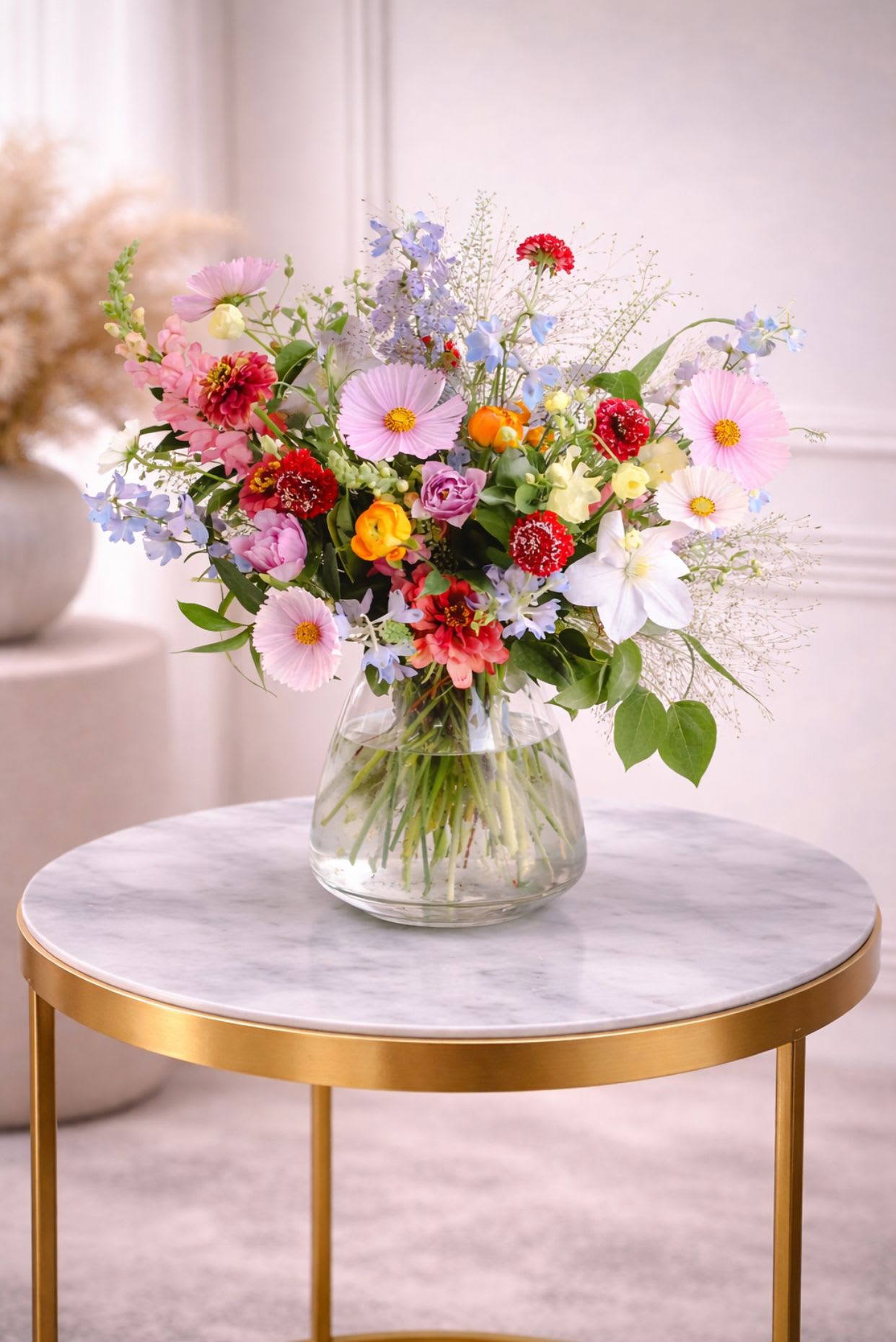 Colorful mixed spring flower arrangement in a clear glass vase on a marble-topped gold table