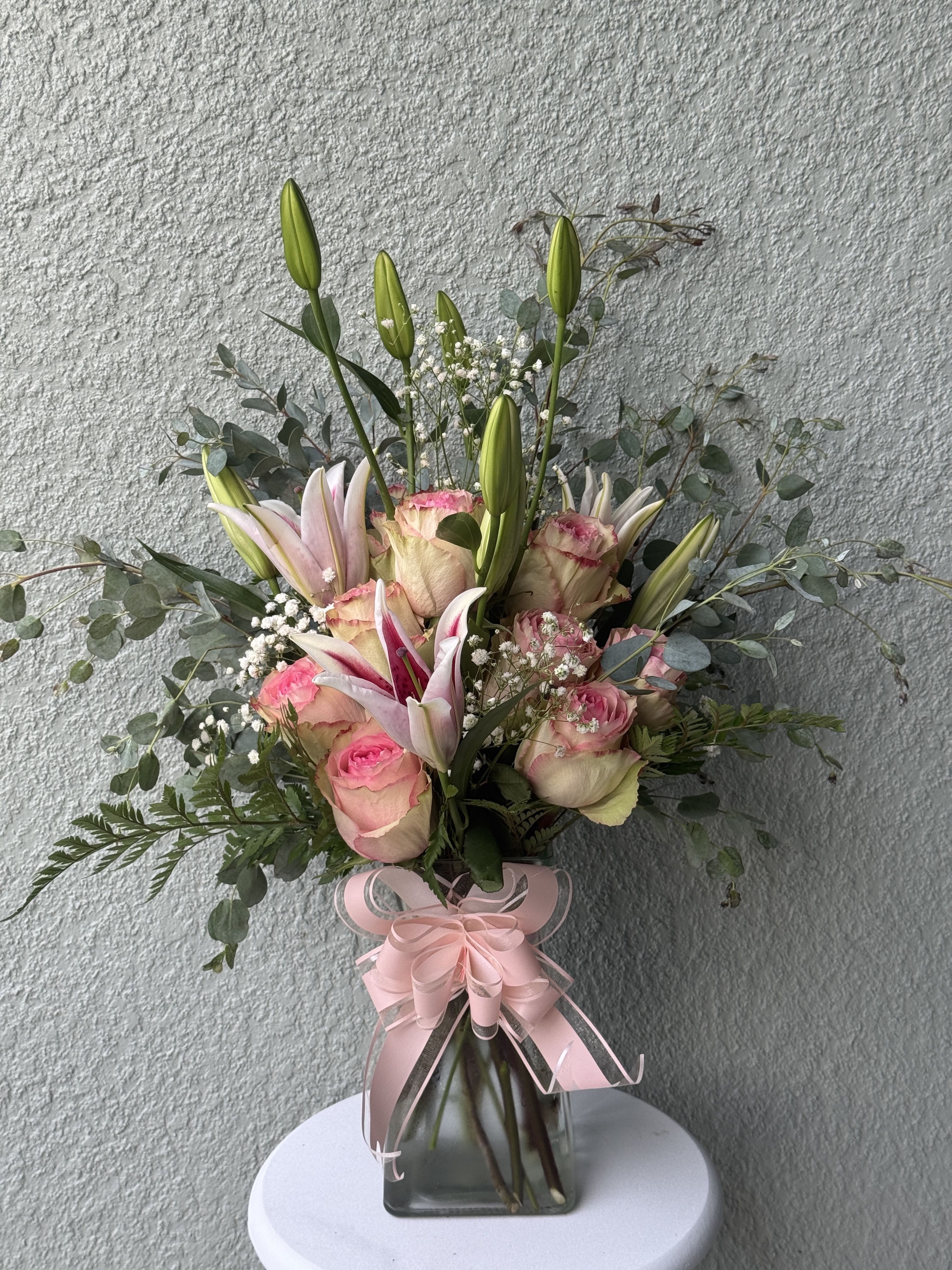 Pink roses and lilies in a glass vase with a pink ribbon