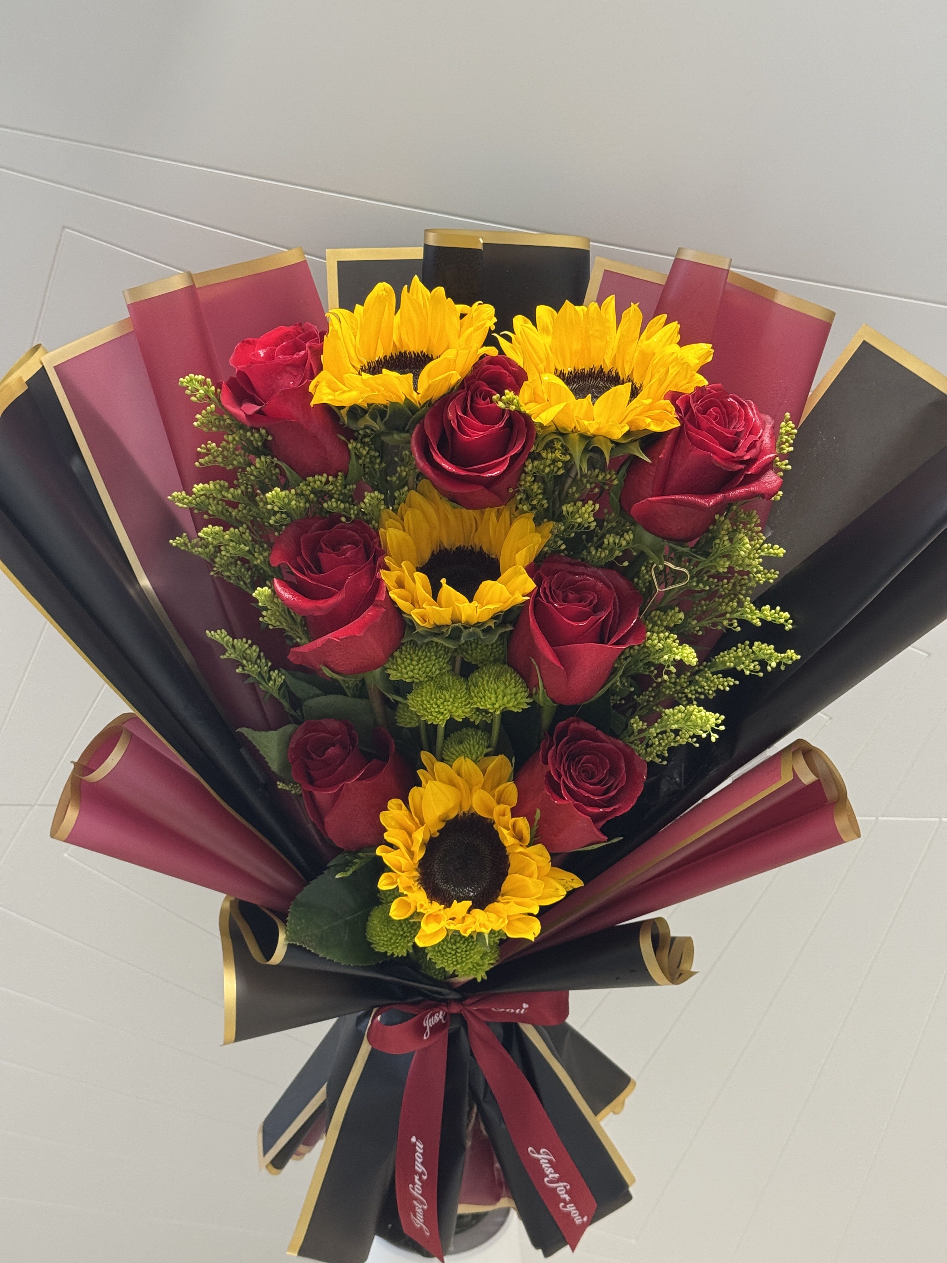 Bouquet of red roses and yellow sunflowers wrapped in black and burgundy paper