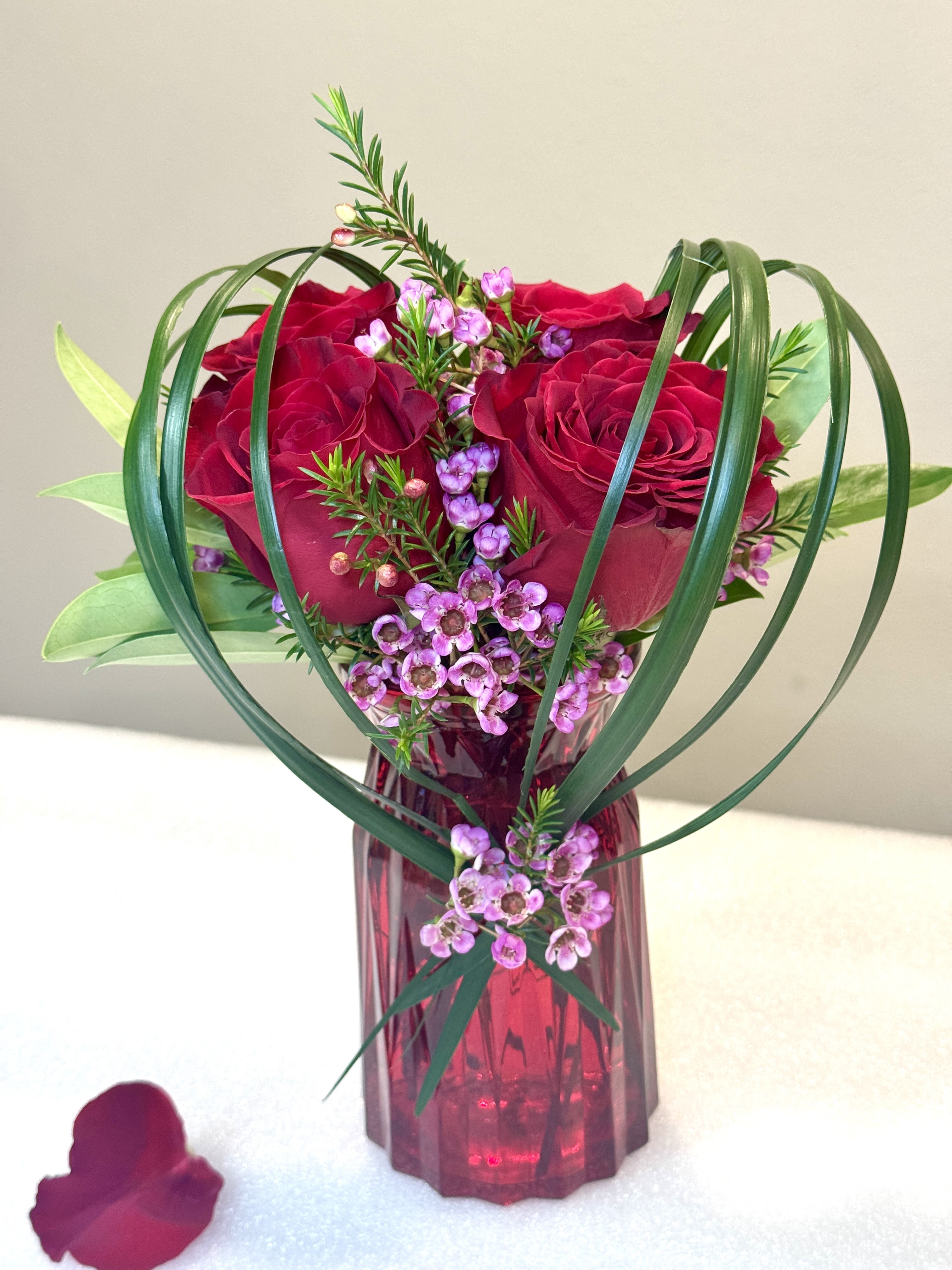 Red roses and pink filler flowers in a red glass vase