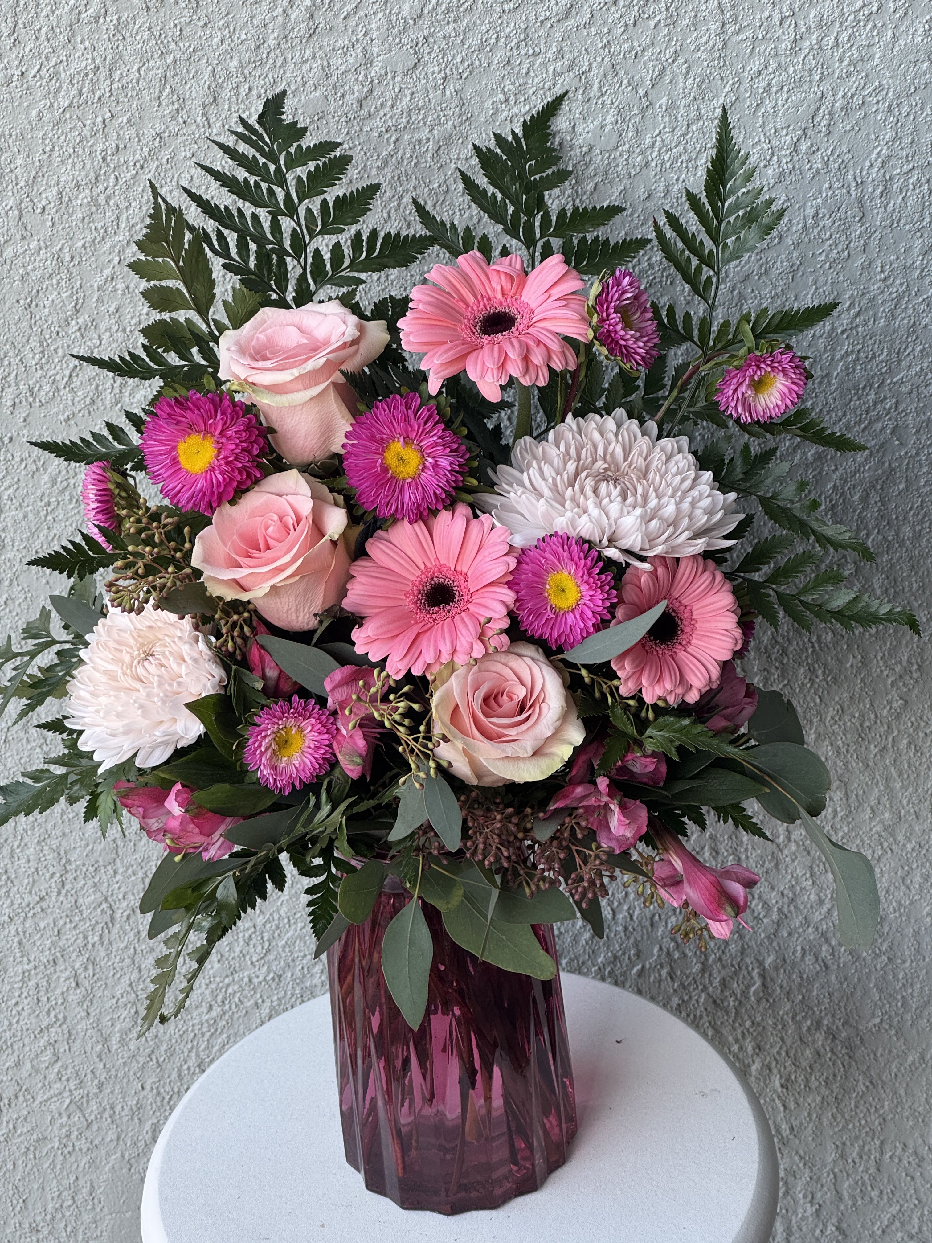 Pink roses and gerbera daisies in a purple glass vase