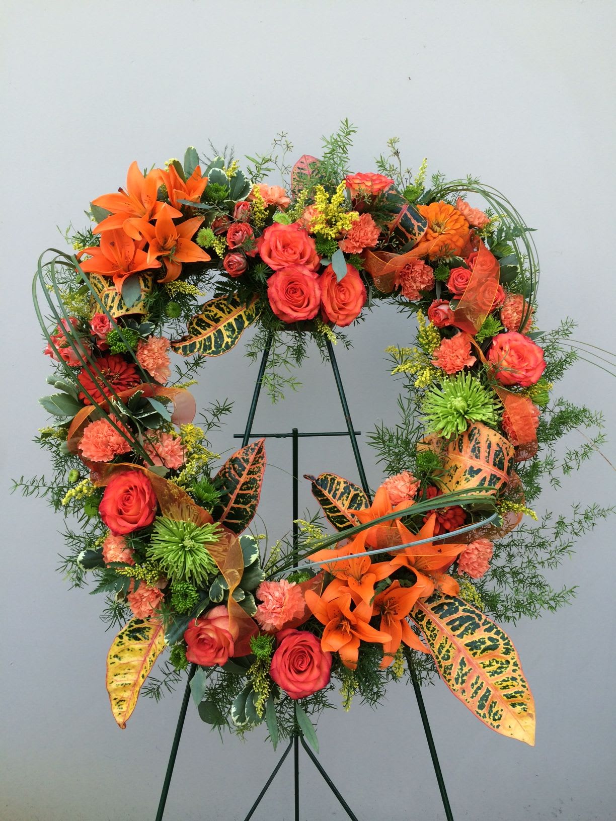 Orange and coral floral wreath on a stand with roses and lilies