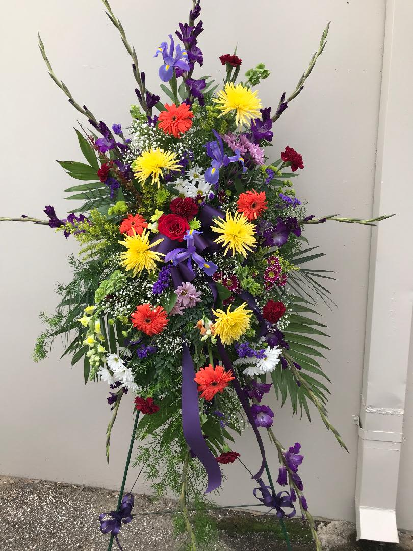 Tall standing floral spray with multicolored blooms and purple ribbon