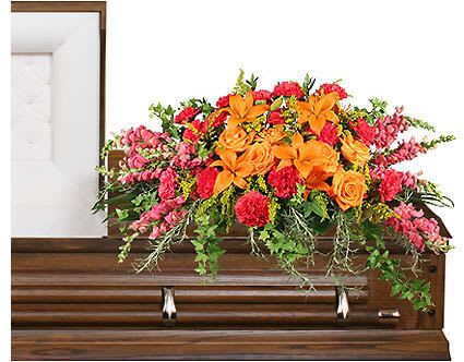 Bright floral spray arranged on top of a wooden casket