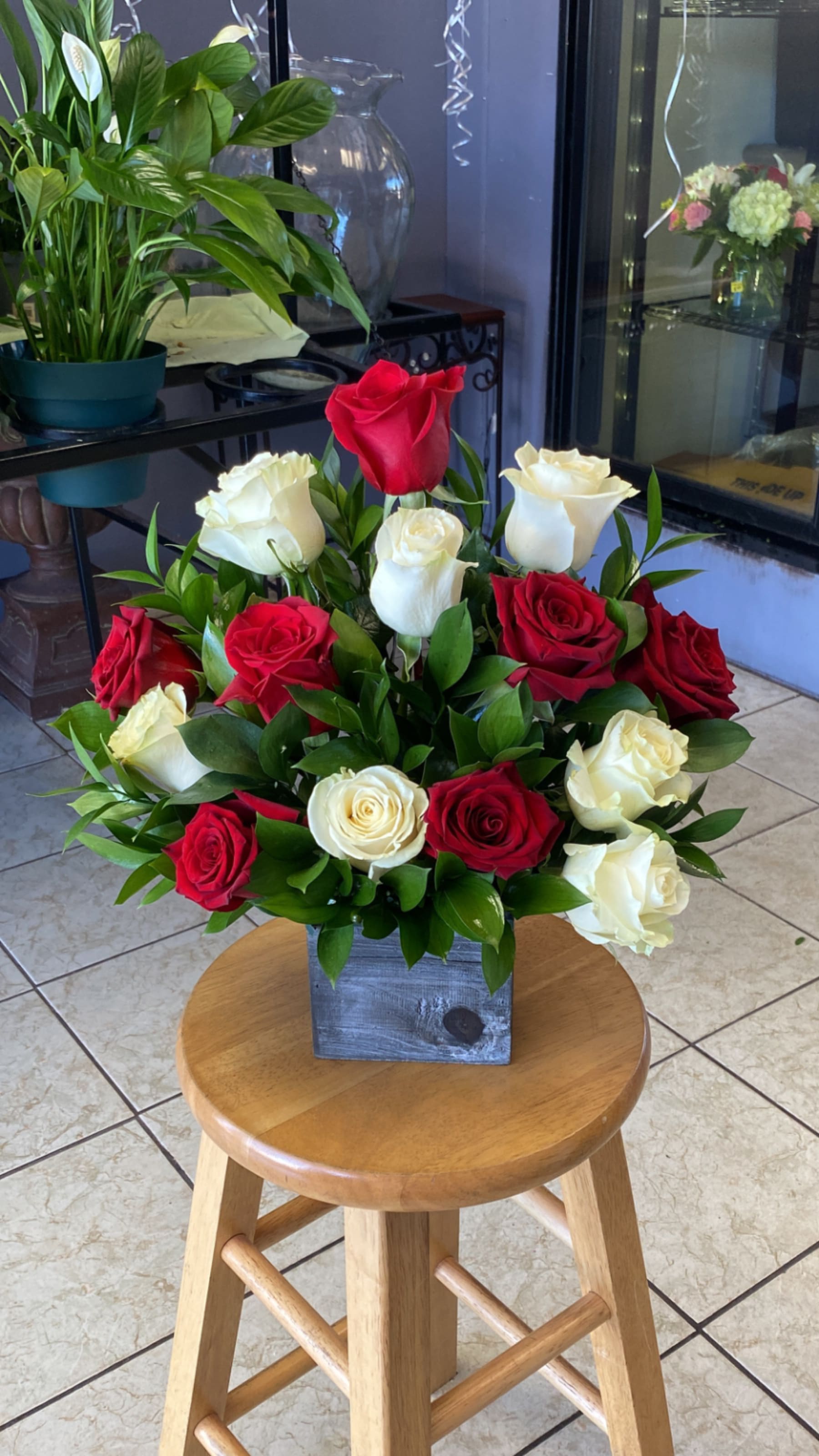 Classic Romance Wooden Box - A compact cluster of red and white roses arranged in a rounded, table-friendly shape in a square wooden vase brings classic romance for anniversaries, Valentine's Day, or a heartfelt thank-you-the glossy green foliage woven between blooms adds texture and clean contrast while the rustic wooden container keeps it simple and ready to display.