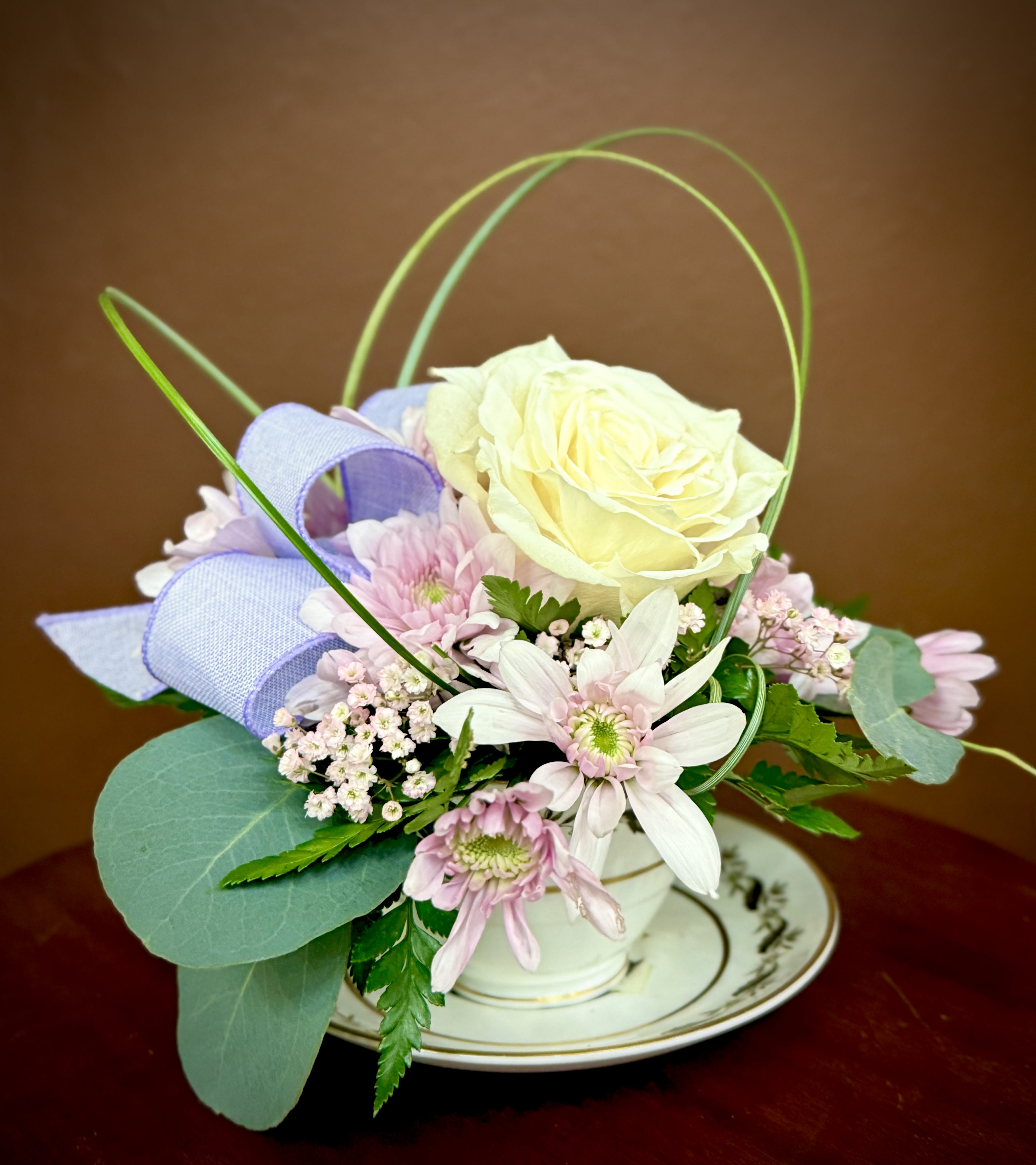 Small pastel flower arrangement in a white cup on a saucer