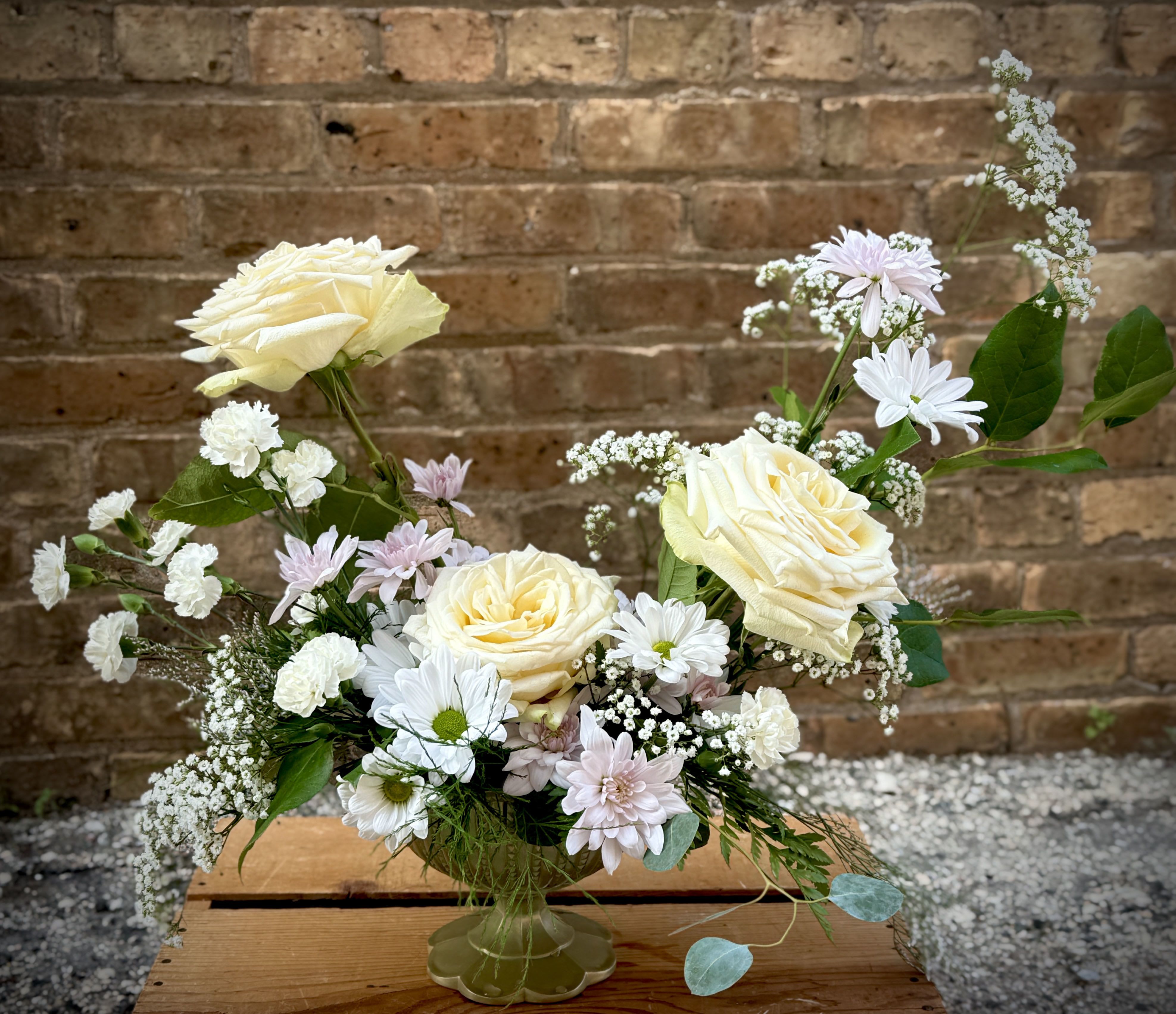 Cream roses and white daisies in a clear vase with pastel filler flowers