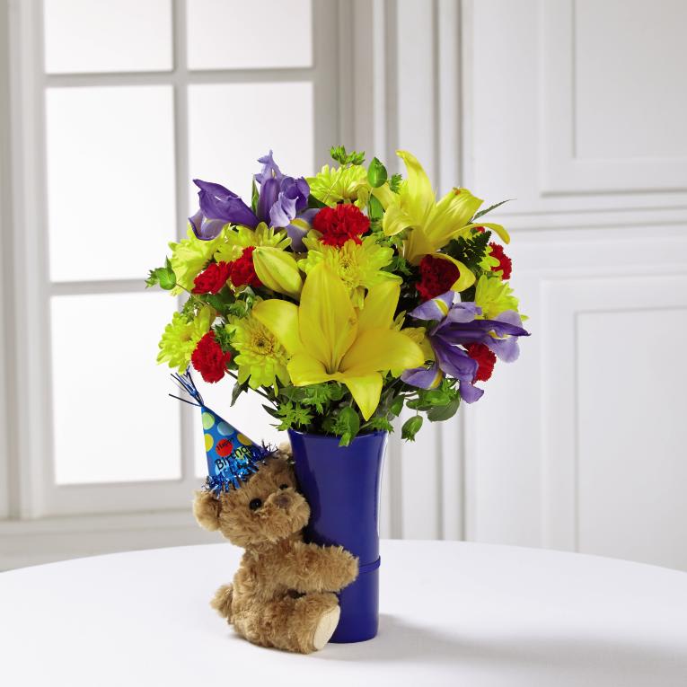 The FTD Big Hug Birthday Bouquet - The FTDÂ¨ Big HugÂ¨ Birthday Bouquet is that perfect way to say "Happy Birthday" to any of the special people in your life in celebration of their big day! Full of color and life to let them know the party has started, this fresh flower arrangement brings together yellow Asiatic Lilies, red roses, red carnations, yellow chrysanthemums, red mini carnations, blue iris, and lush greens to create an eye-catching display. Presented in a blue ceramic vase with a plush brown bear donning a party hat sweetly hugging it tightly on the side, this birthday bouquet is a unique gift blooming with festive fun and love at every turn. GOOD bouquet includes 8 stems. Approx. 15"H x 11"W. BETTER bouquet includes 14 stems. Approx. 16"H x 12"W. BEST bouquet includes 19 stems. Approx. 17"H x 14"W. EXQUISITE bouquet includes 23 stems. Approx. 18"H x 14"W.