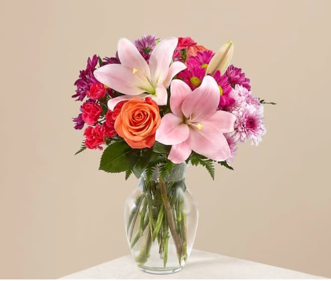 Light of My Life Bouquet - The Light of My Life Bouquet blossoms with brilliant color and a sweet sophistication to create the perfect impression! Pink Lilies make the eyes dance across the unique design of this flower bouquet, surrounded by the blushing colors of orange roses, lavender cushion poms, hot pink carnations, and lush greens. Presented in a clear glass vase, this fresh flower arrangement has been created just for you to help you send your sweetest thank you, happy anniversary, or thinking of you wishes. 