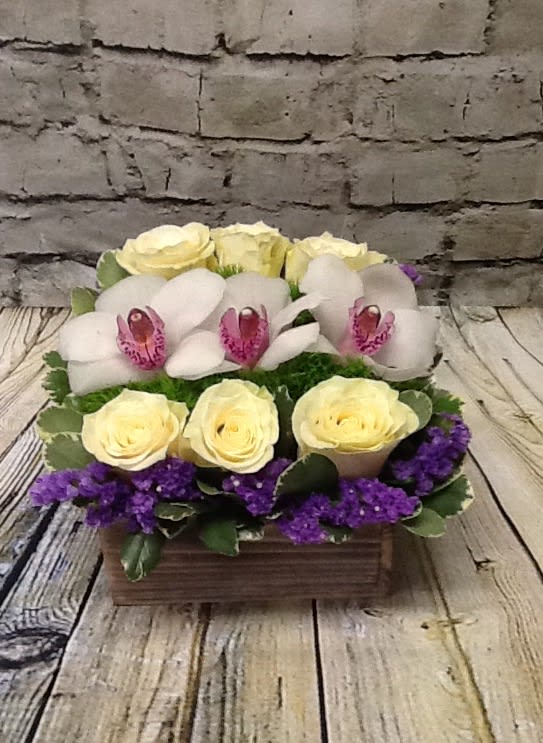 Arrangement of pale yellow roses, white orchids, and purple filler in a wooden box