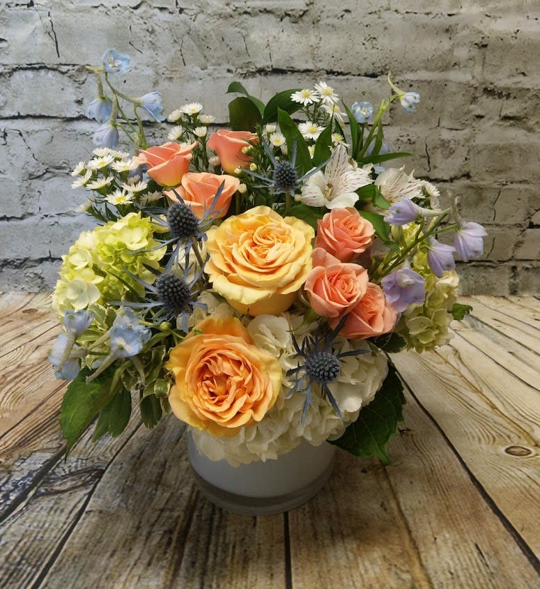 Mixed bouquet of peach roses, hydrangeas, and blue thistle in a white vase