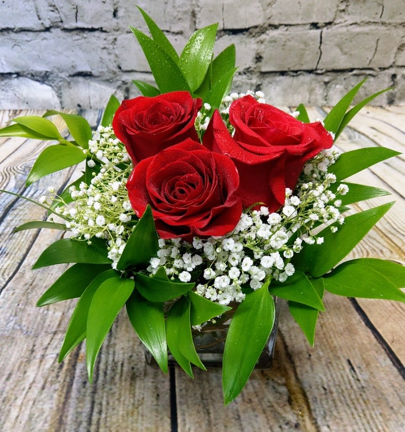 Three red roses in a low glass vase with white filler flowers