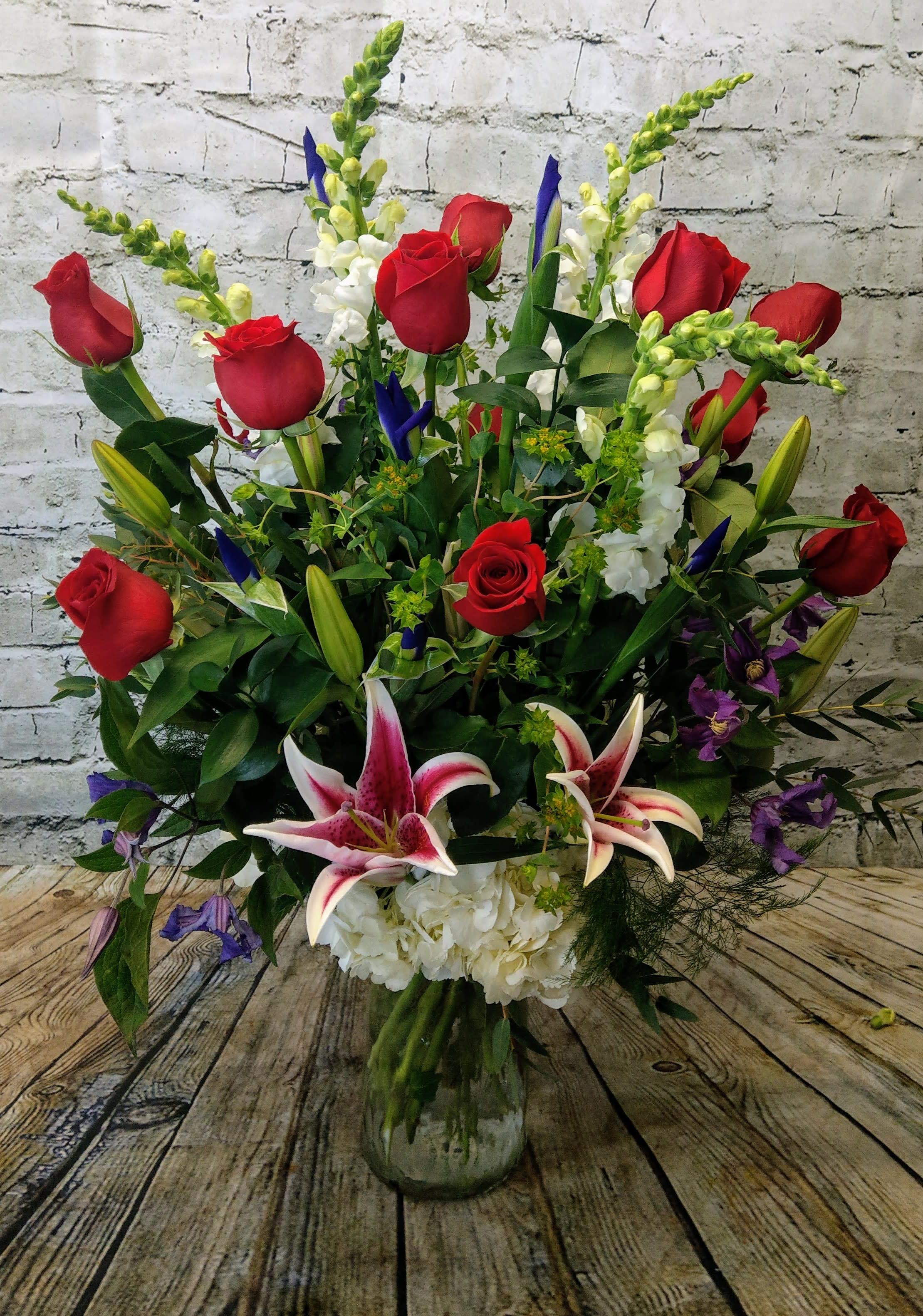 Large bouquet of red roses, white lilies, and purple flowers in a glass vase