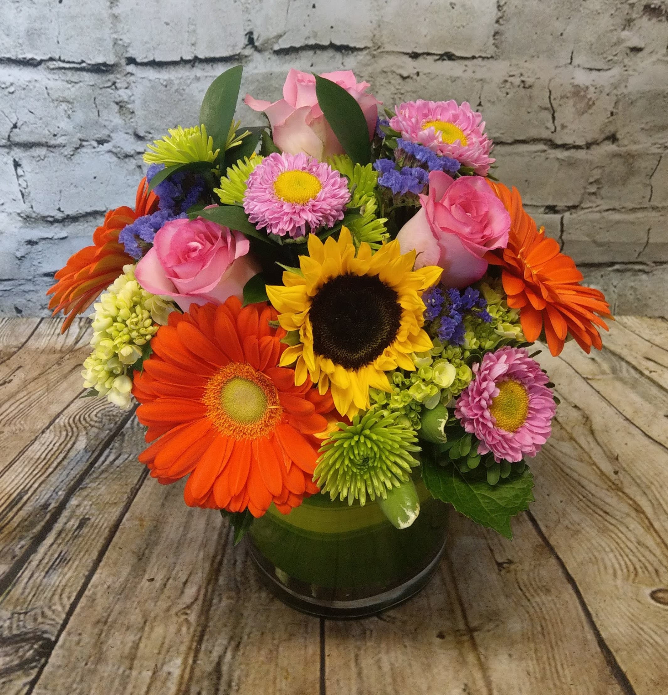 Mixed bouquet with pink roses, sunflowers, and colorful daisies in a glass vase