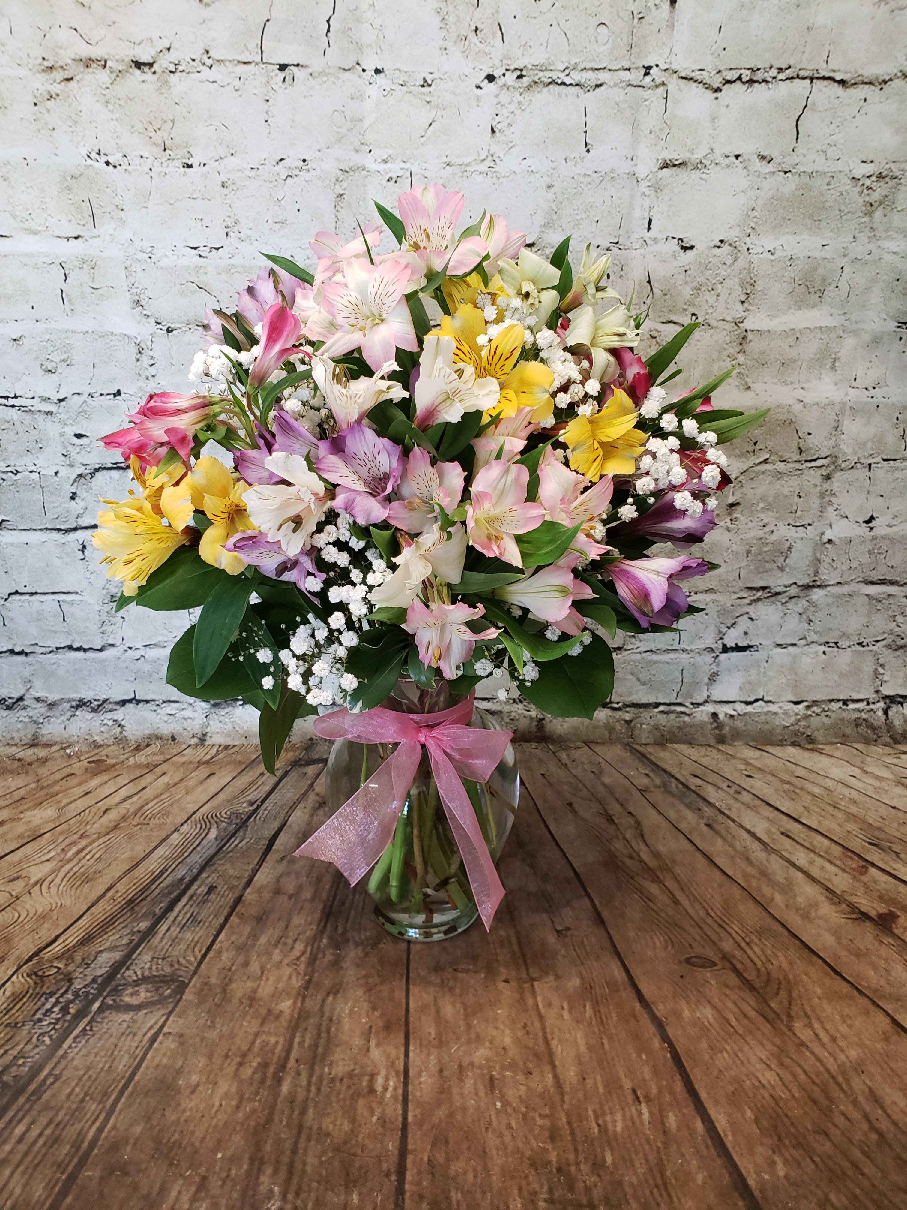 Mixed pink, yellow, and white flowers in a glass vase with a pink ribbon