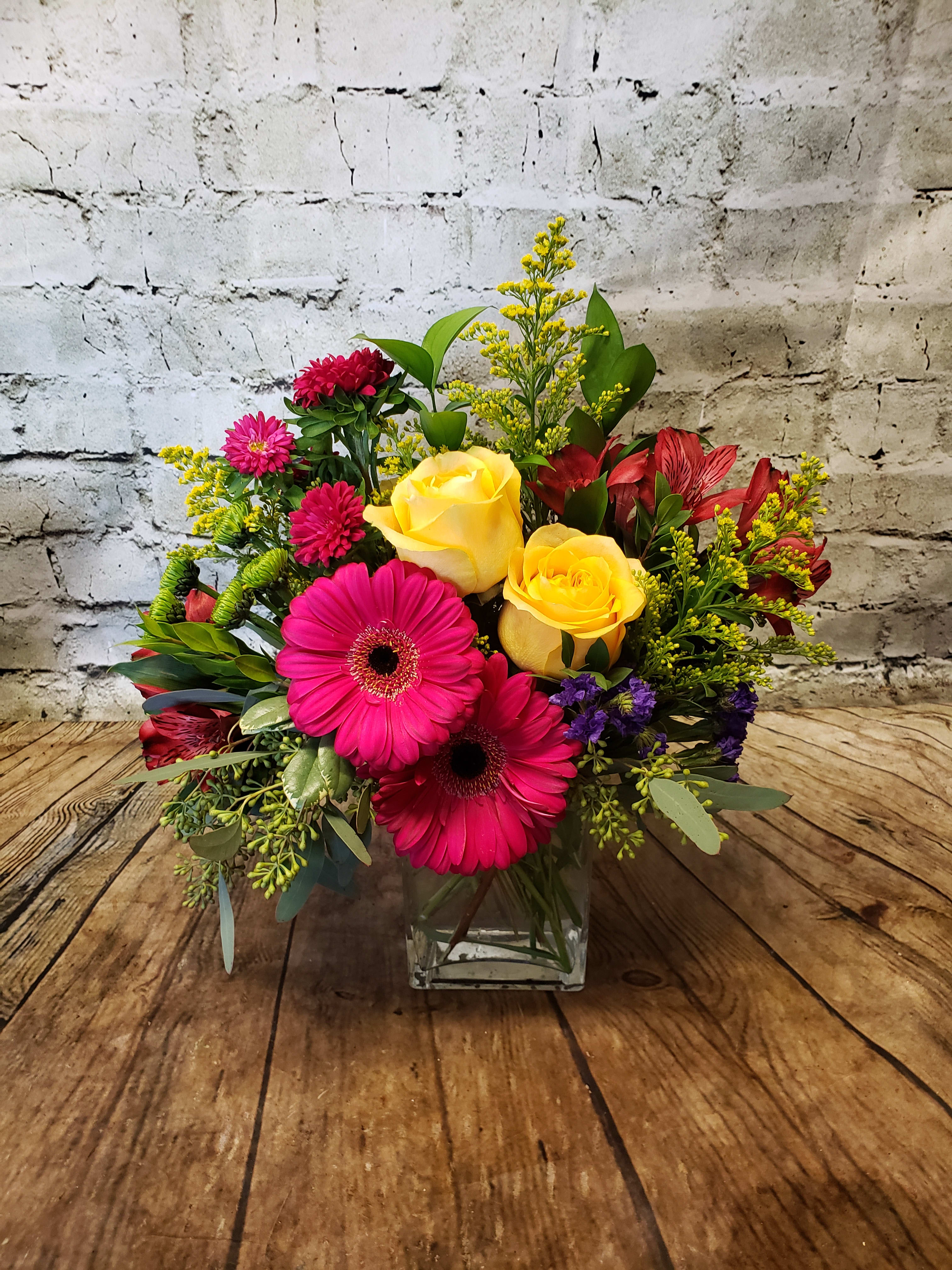 Bright mixed bouquet with yellow roses and pink gerbera daisies in a glass vase