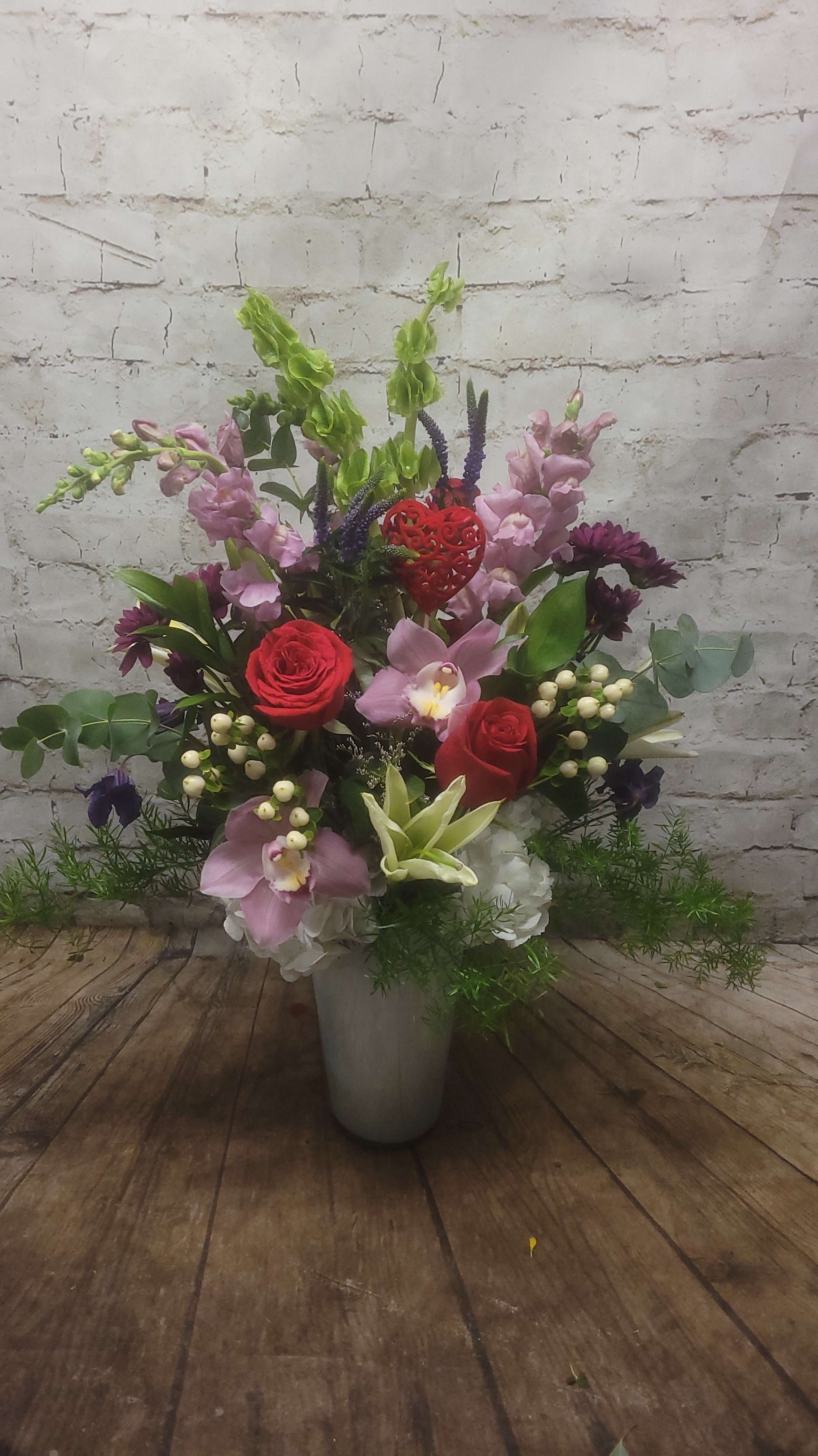 Mixed floral arrangement in a gray vase with red roses and pink orchids