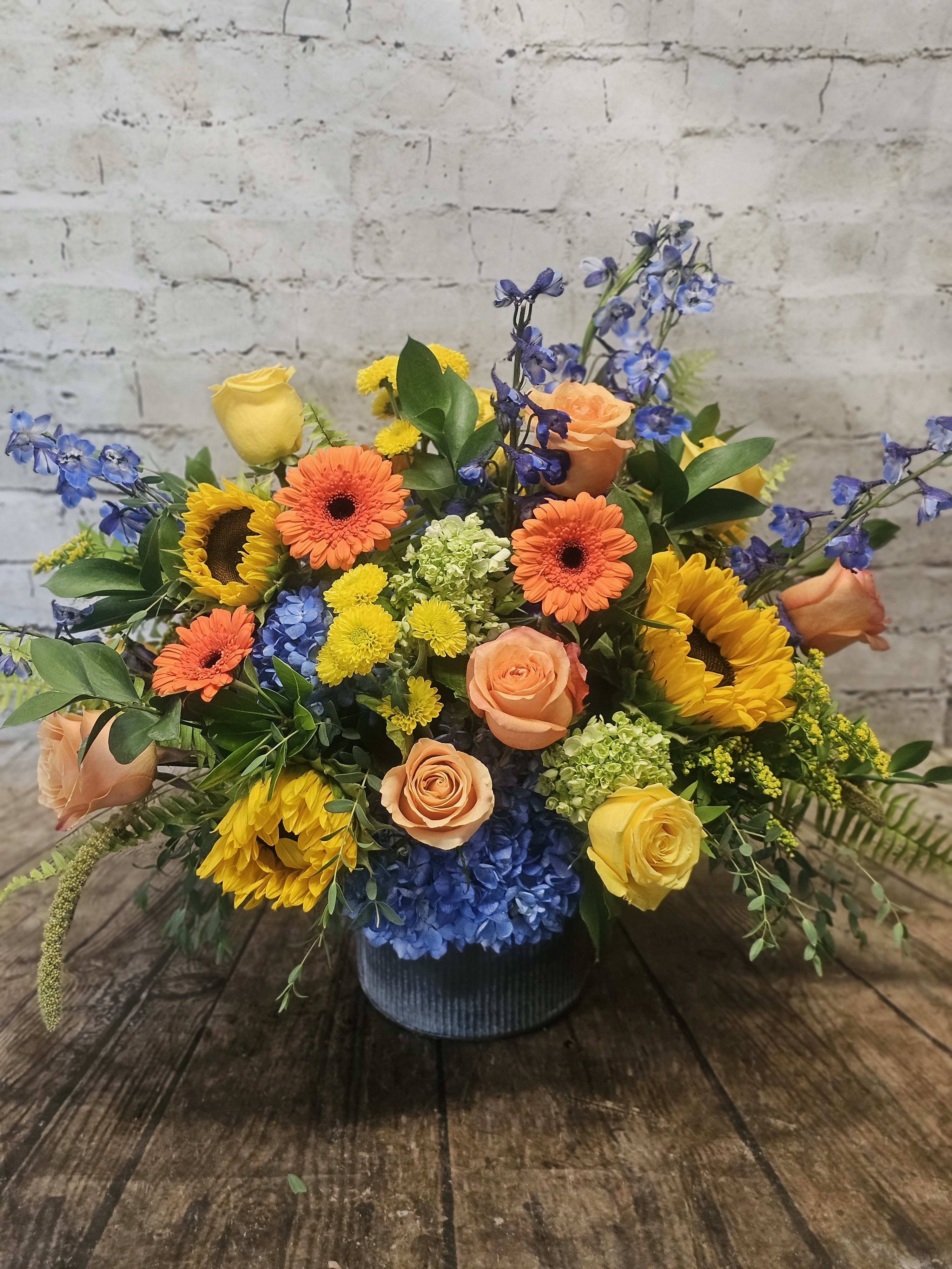 Mixed bouquet of roses, sunflowers, gerbera daisies, and blue hydrangeas in a vase