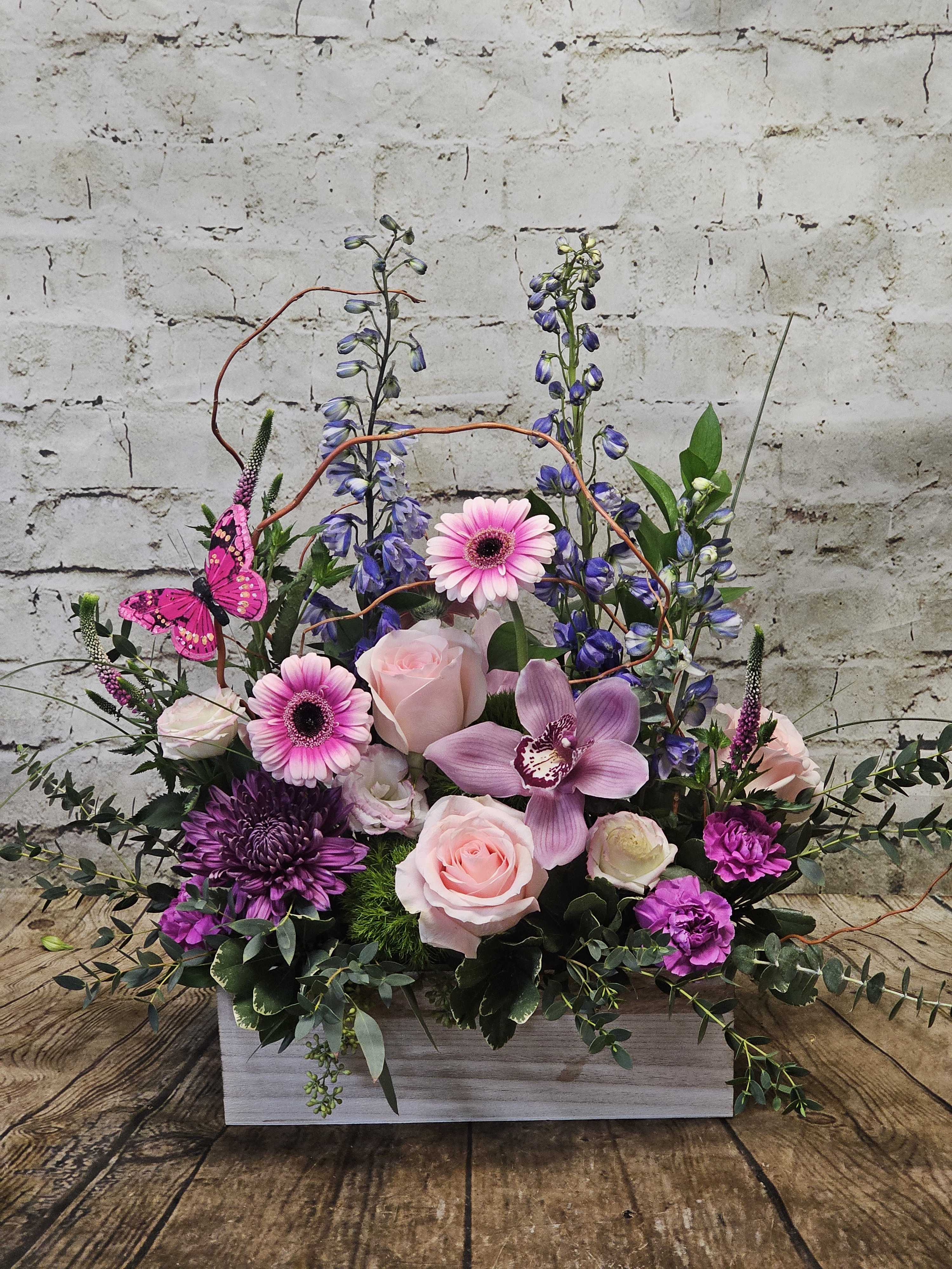 Pink and purple floral arrangement in a white wooden box with a butterfly accent