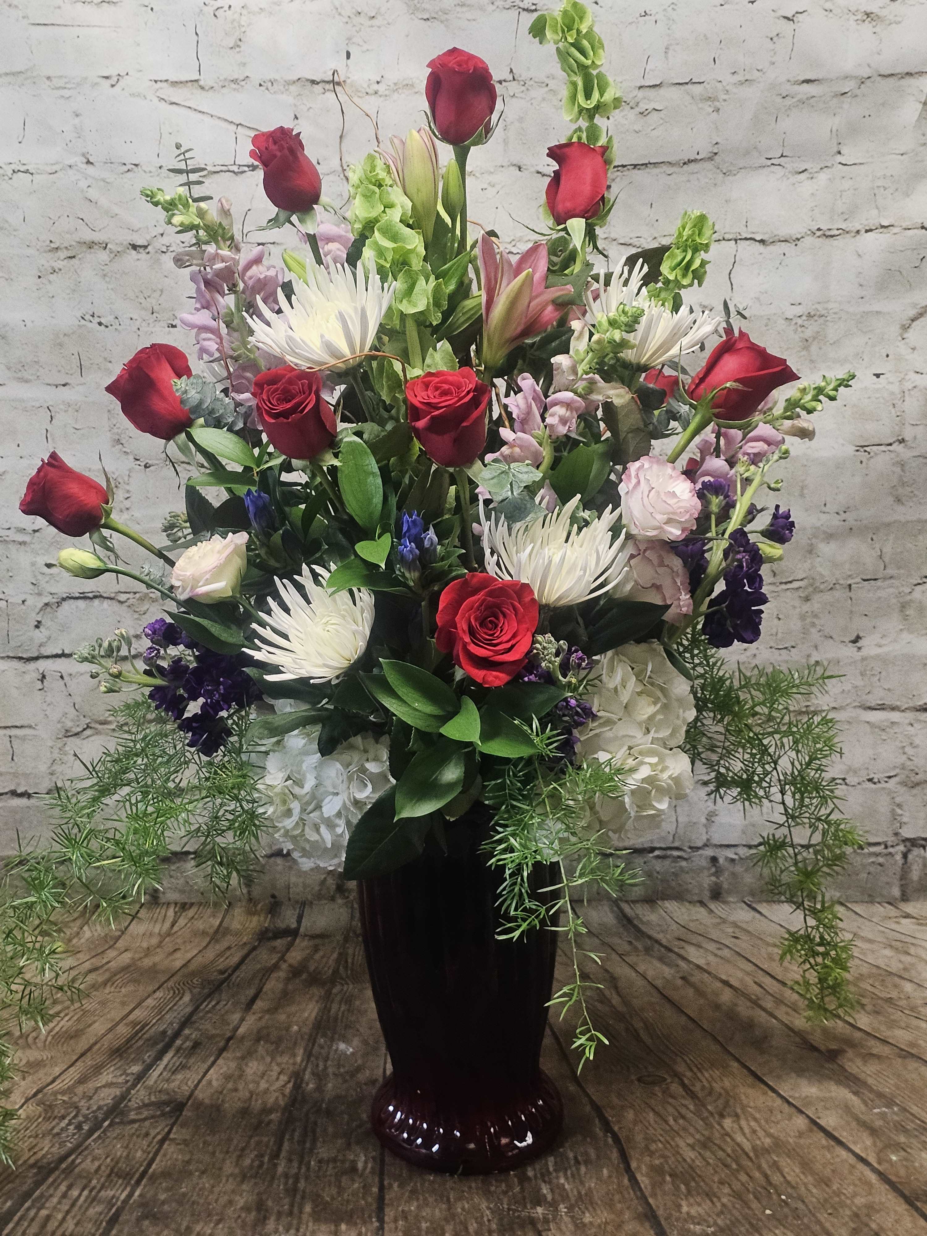Tall vase arrangement with red roses, white spider mums, and mixed blooms