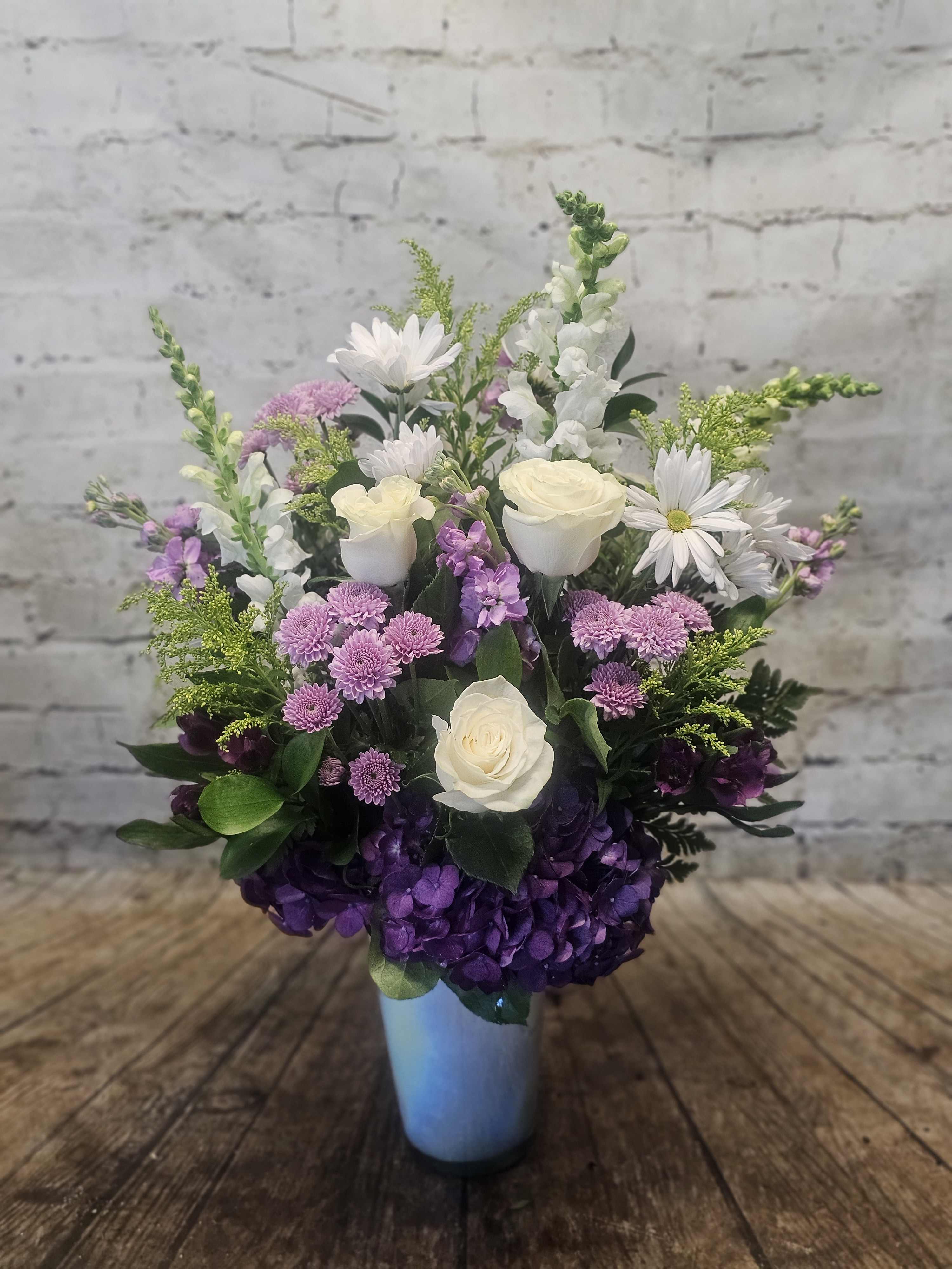 Mixed bouquet in a blue vase with white roses, purple hydrangea, and daisies