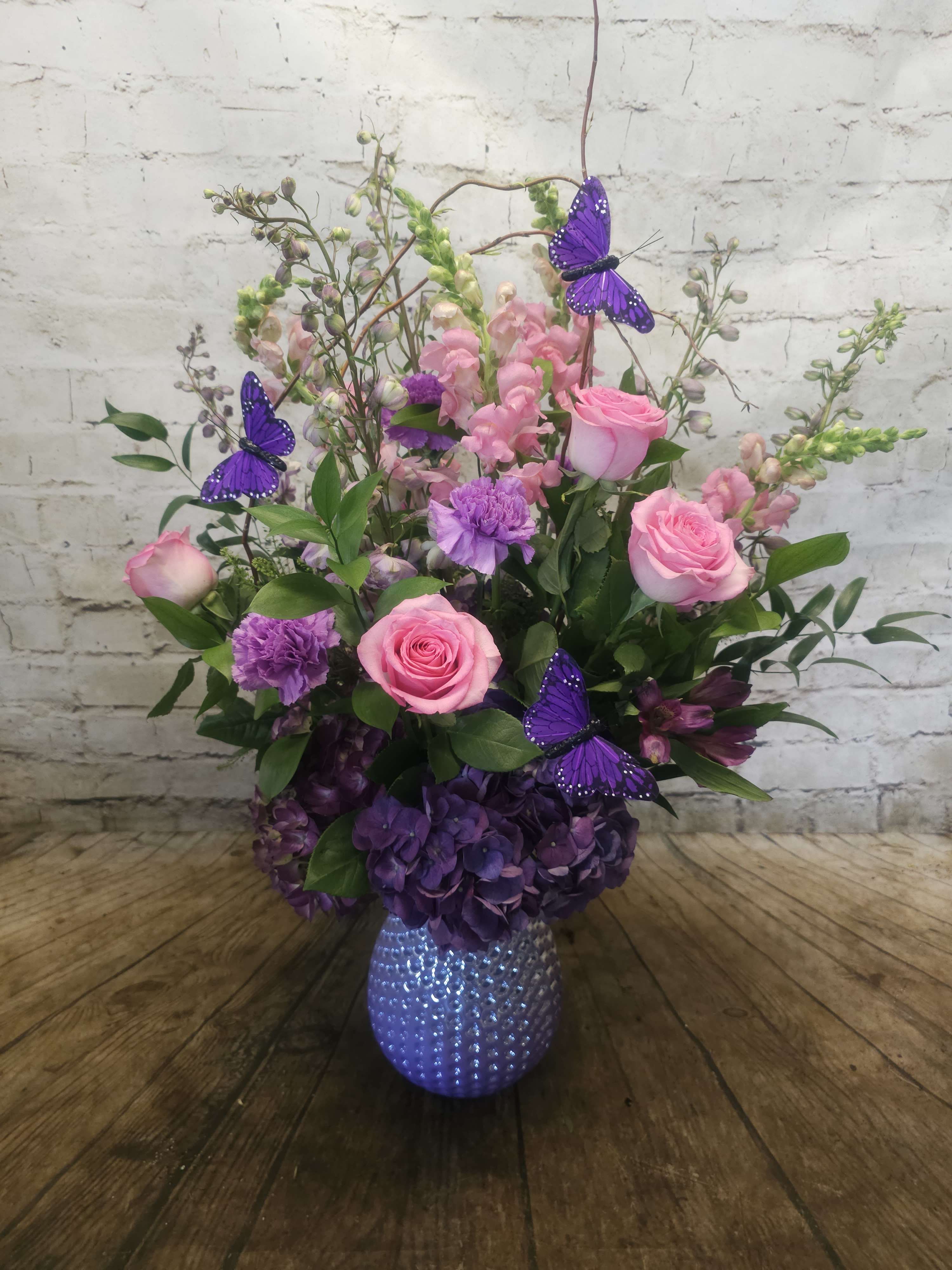 Pink roses and purple flowers in a textured vase with butterfly picks