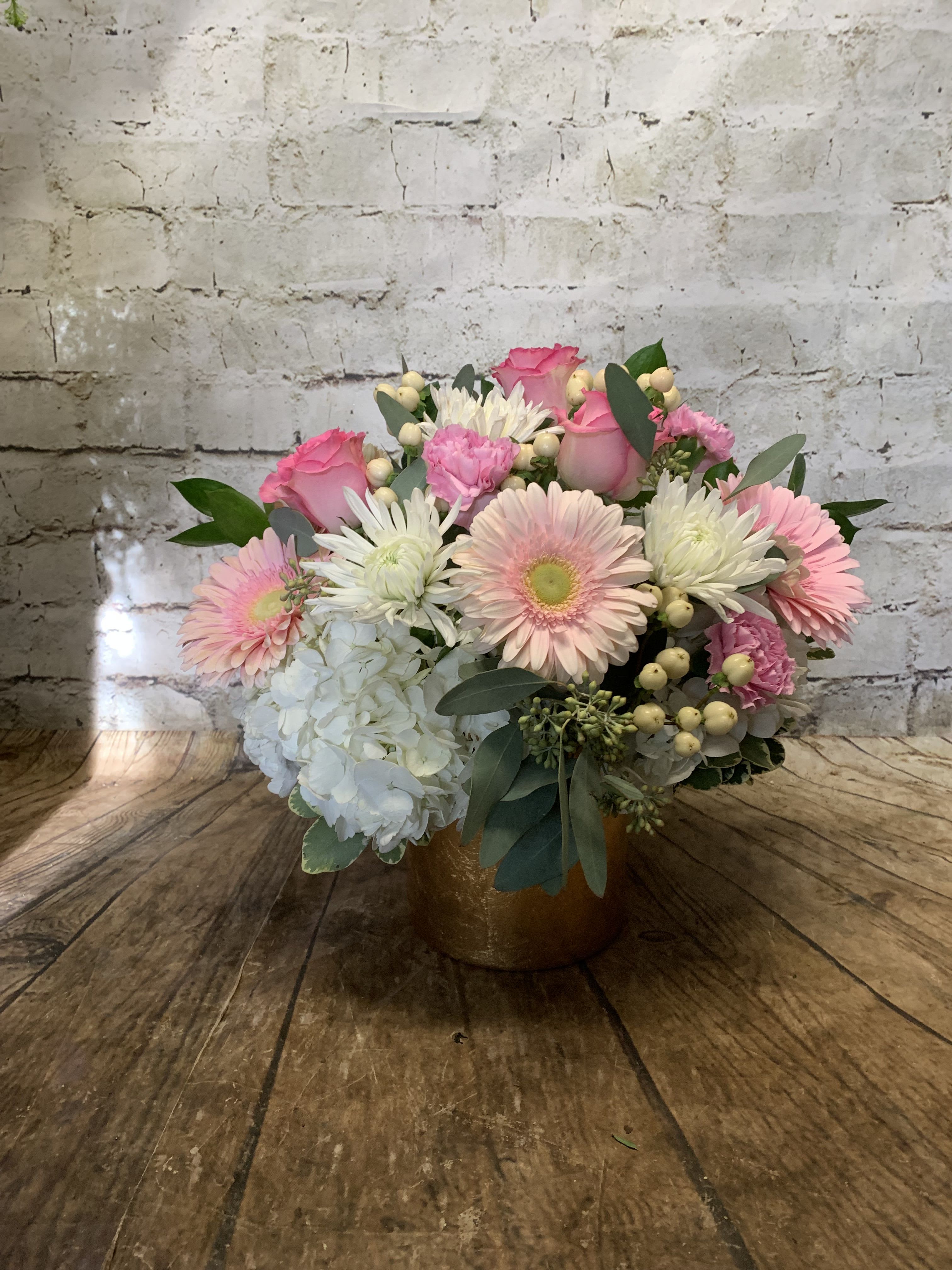 Pink roses and gerbera daisies in a gold vase with white hydrangea