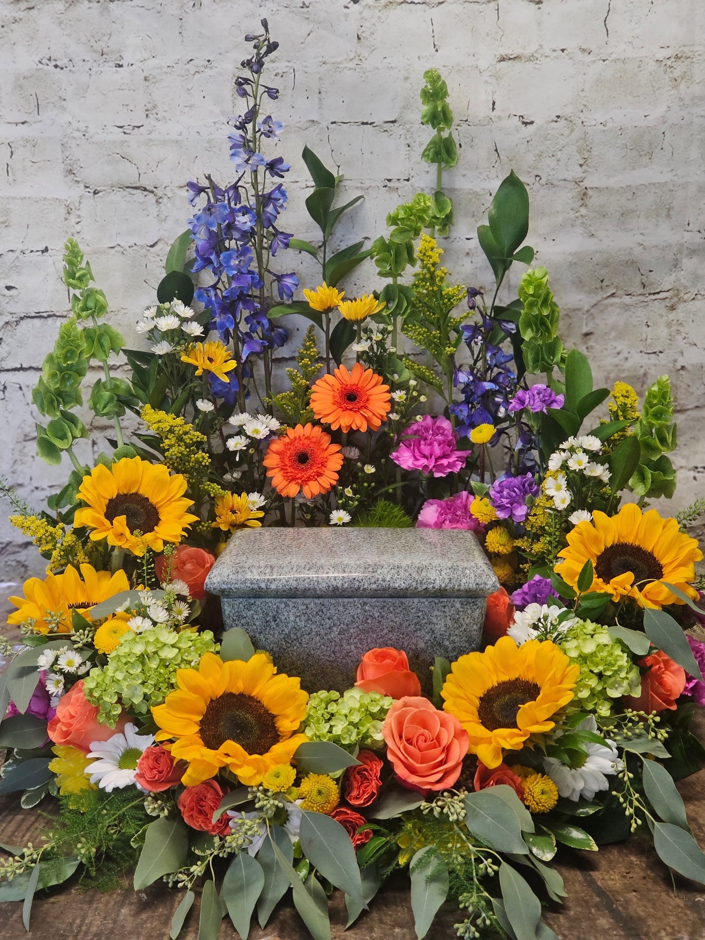 Colorful funeral spray around a gray granite urn with sunflowers and roses