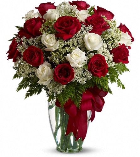 Red and white roses in a clear glass vase with a red ribbon