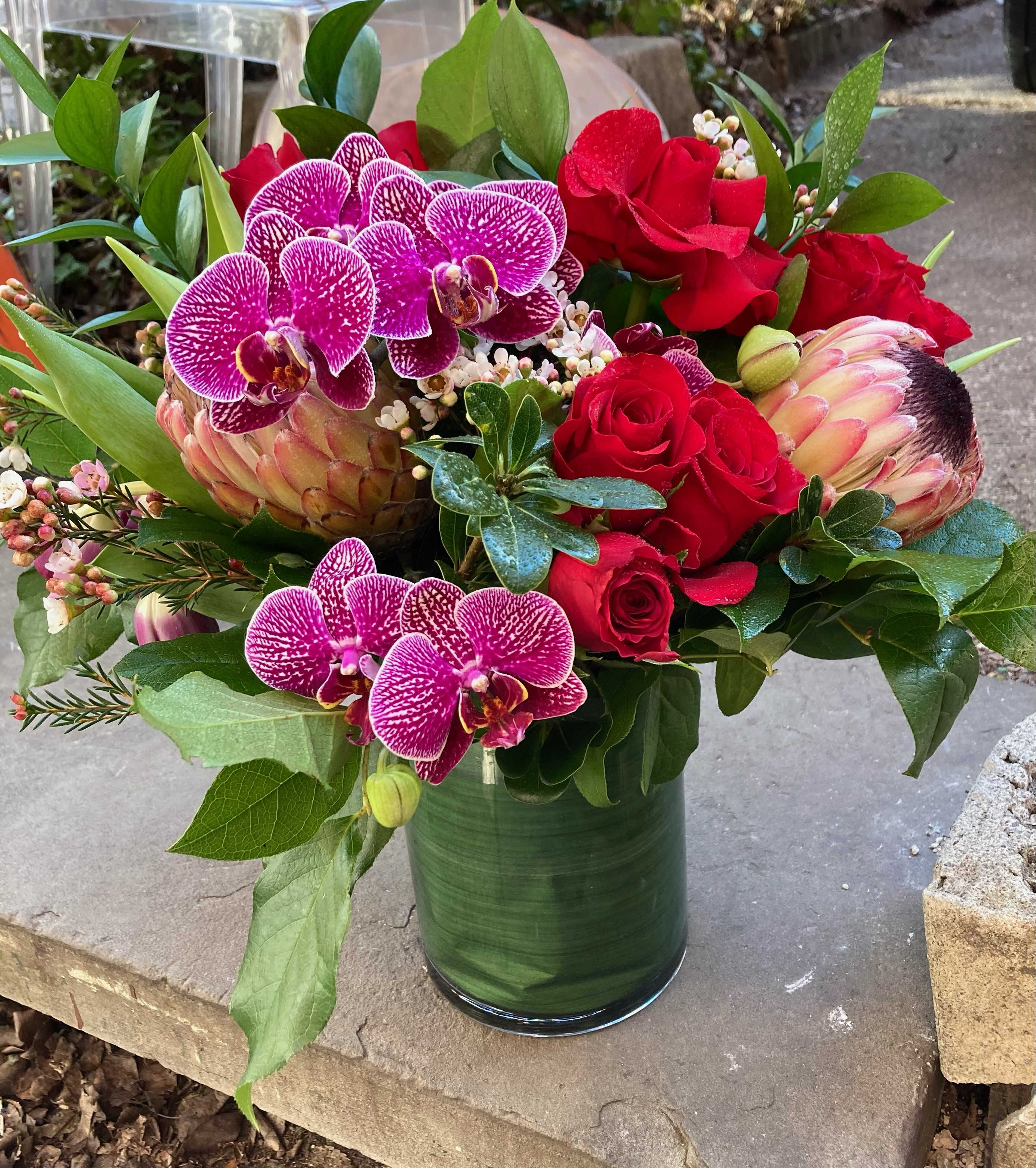 Bouquet of red roses and purple orchids in a green glass vase