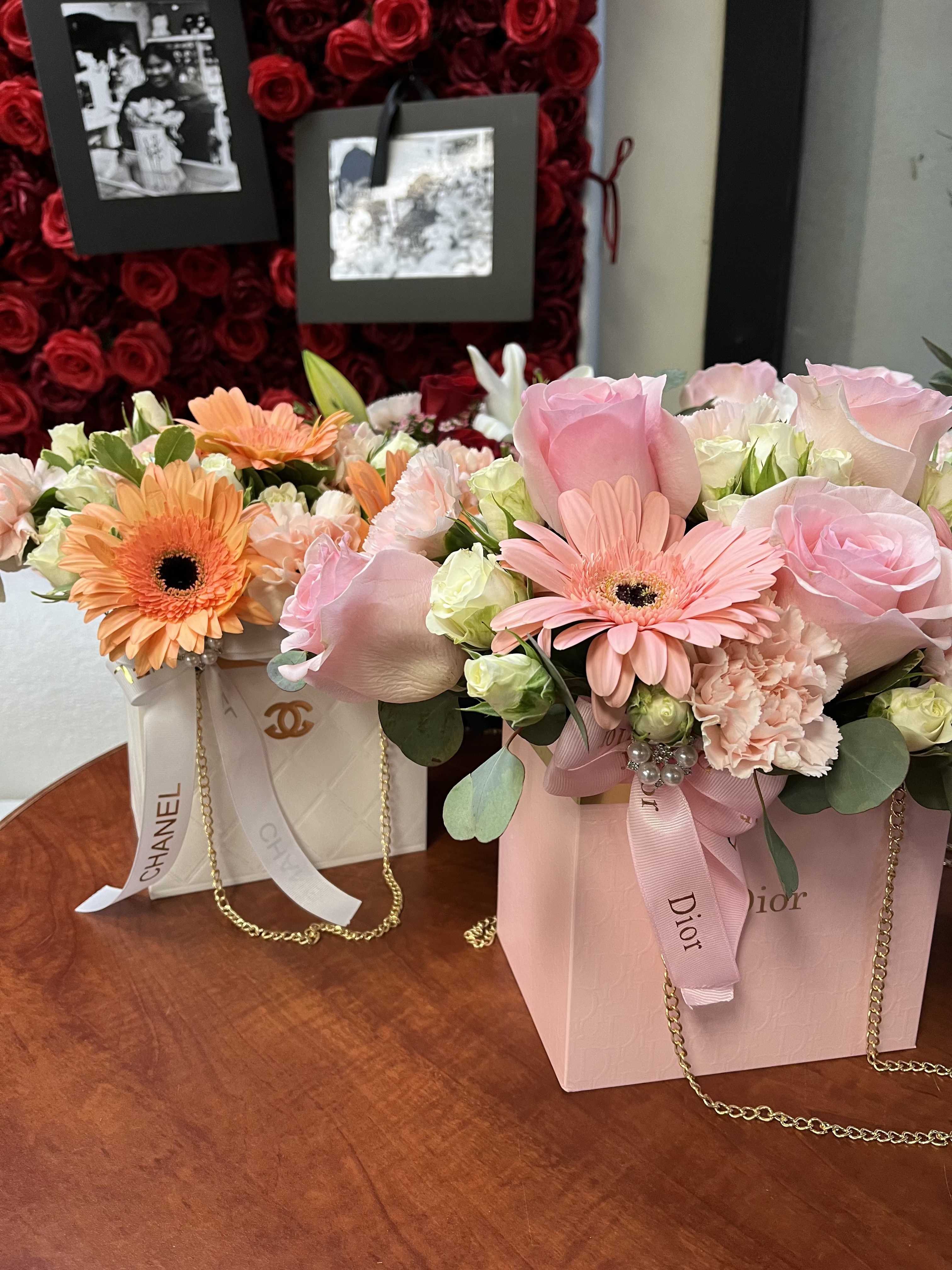 Two pastel flower arrangements in branded gift boxes with ribbon and chain handles.