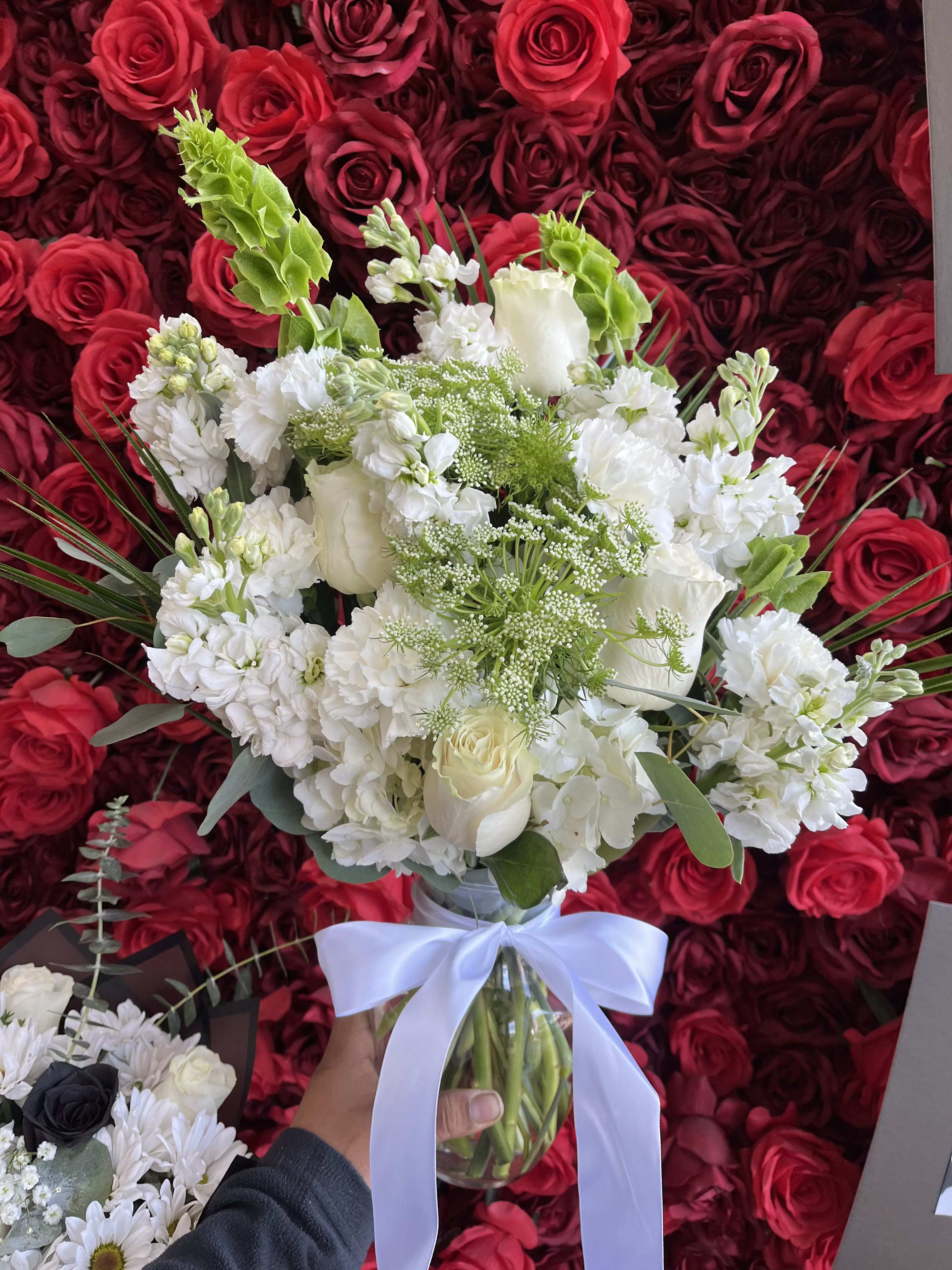 White bouquet in a glass vase with a white ribbon, set against red roses