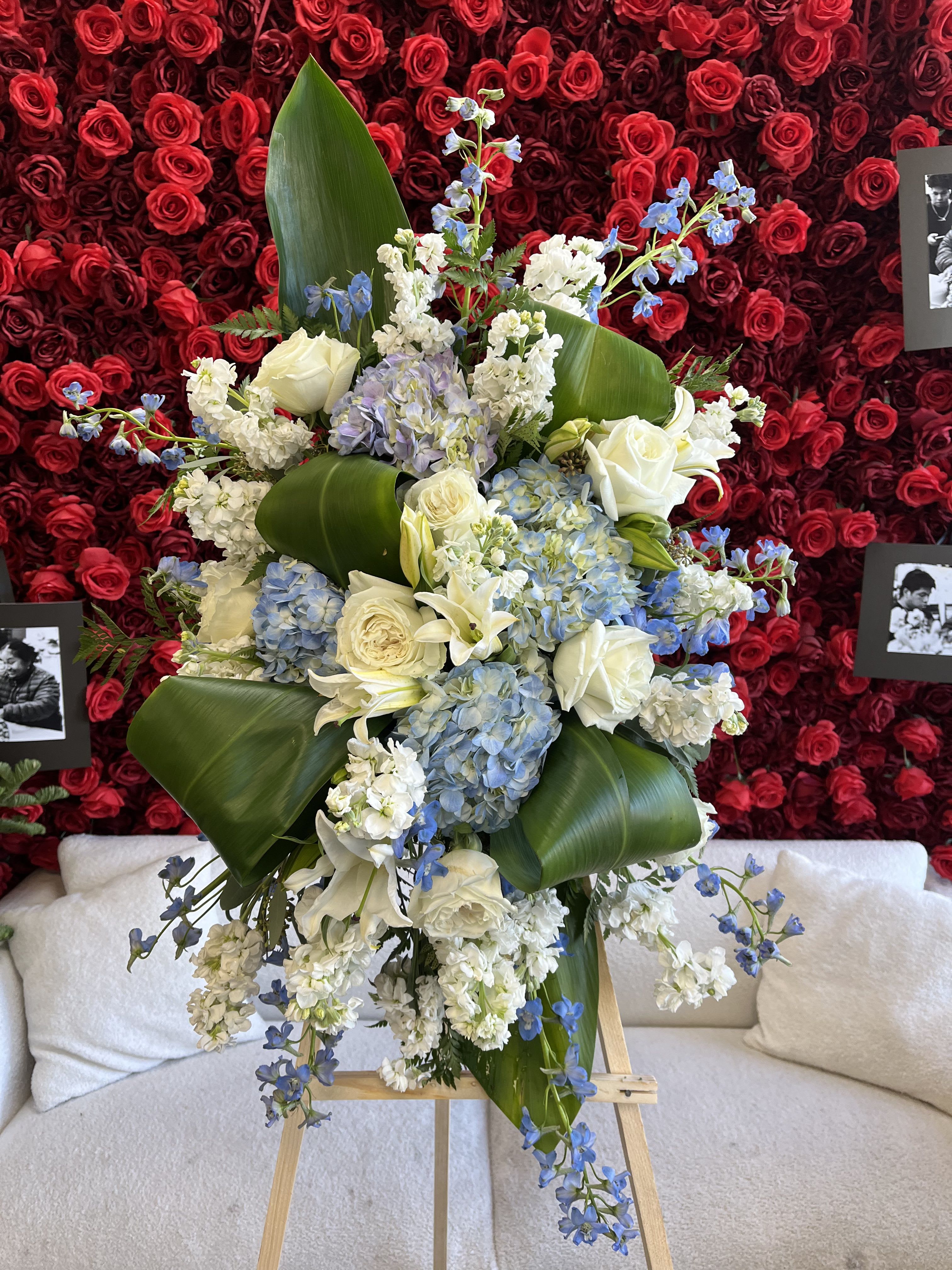 Large floral spray with white roses, blue blooms, and broad green leaves