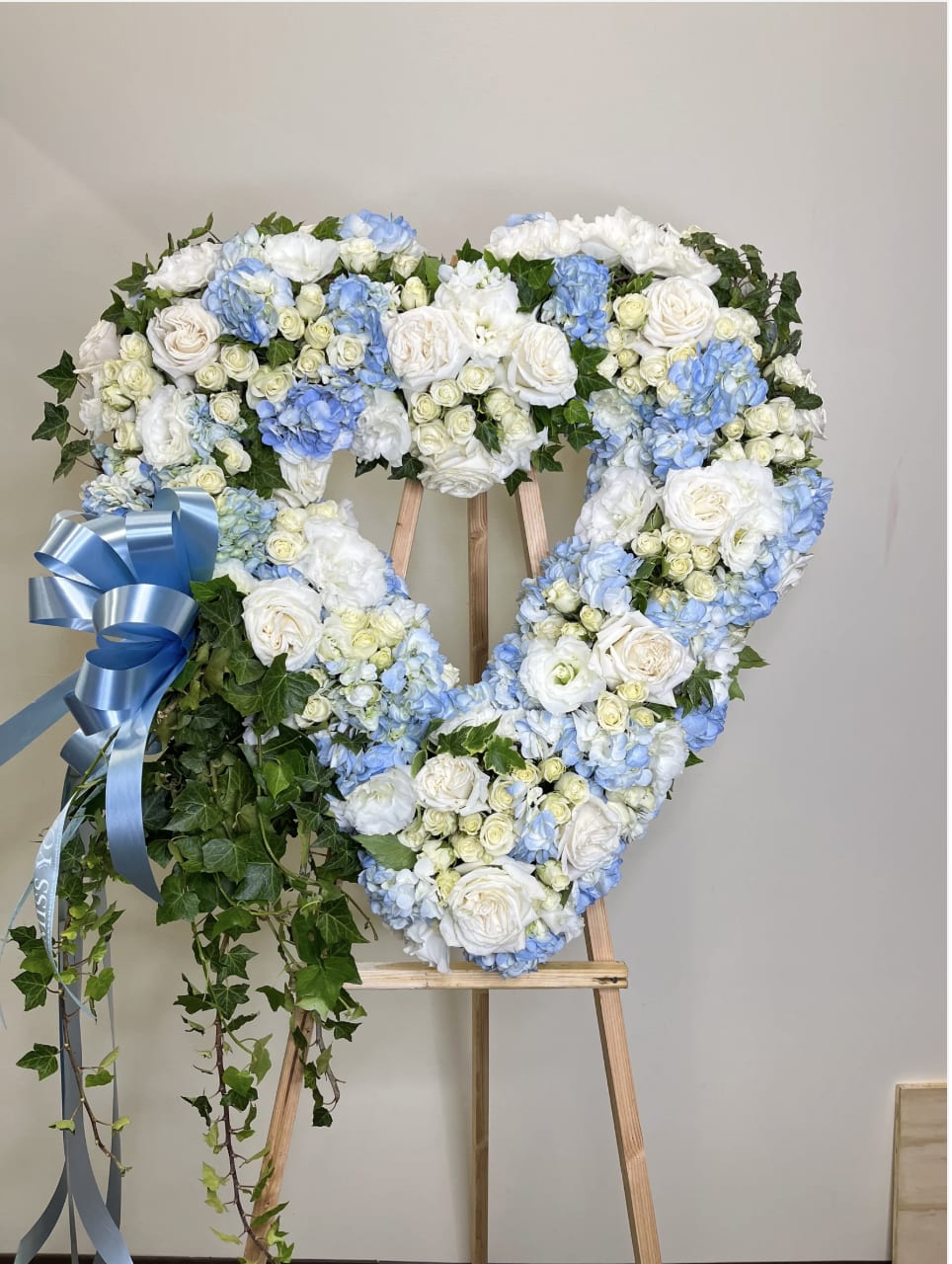 Heart-shaped floral wreath of white and blue flowers on an easel with a blue ribbon