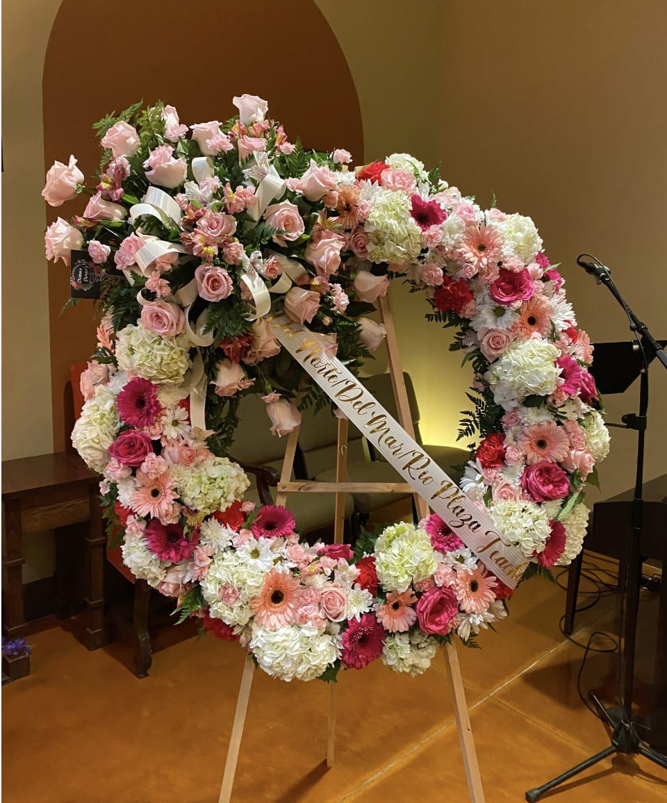 Large pink and white floral wreath on an easel with a memorial ribbon