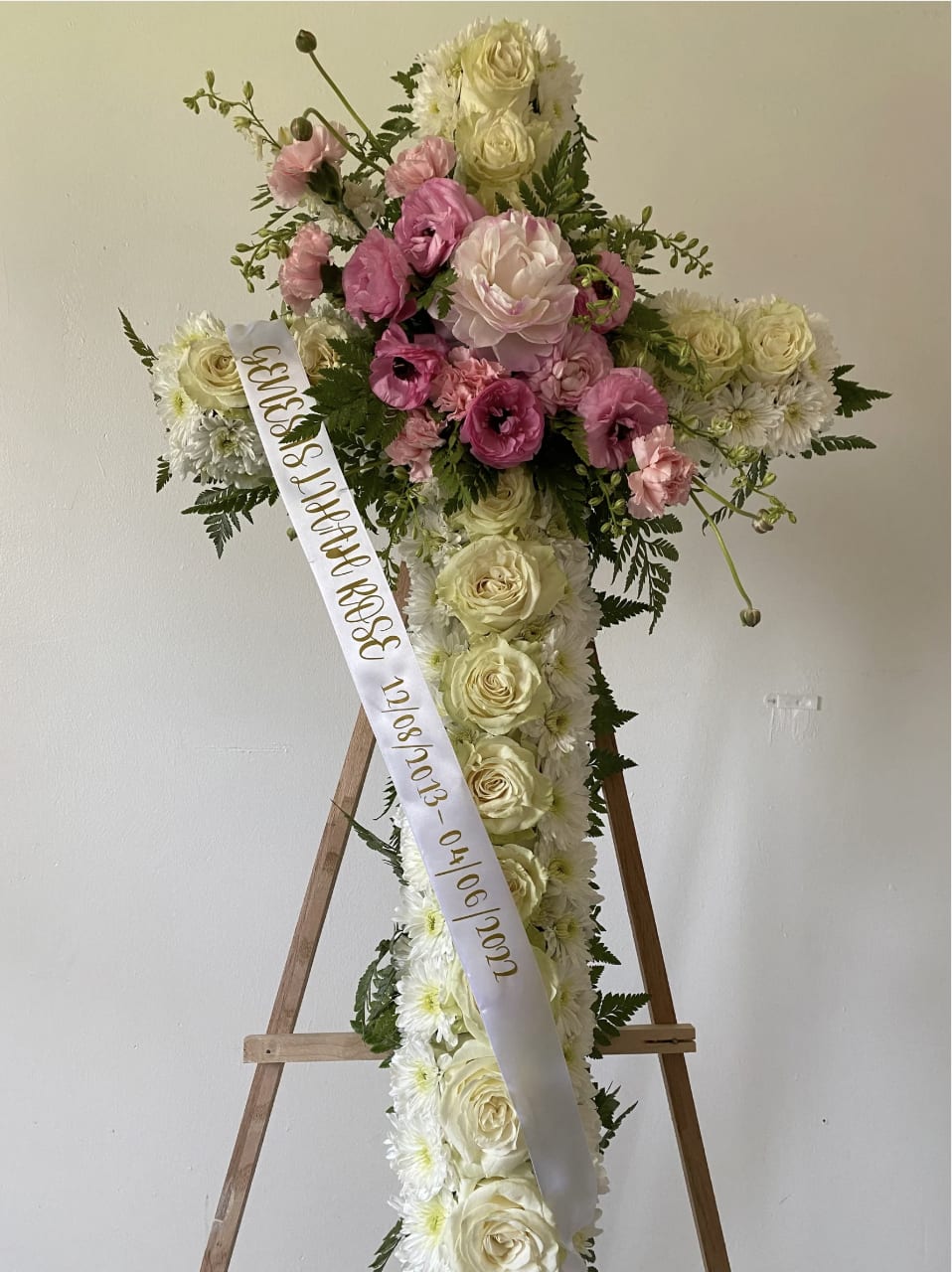 Cross-shaped floral tribute with pink and white roses on an easel