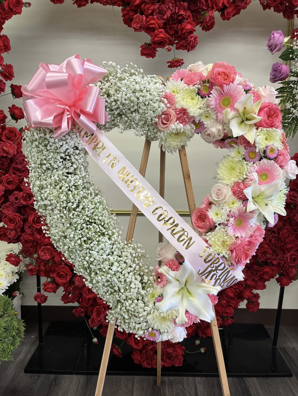 Heart-shaped floral wreath on an easel with pink and white flowers and a ribbon