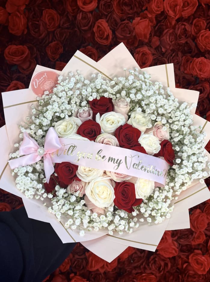 Bouquet of red, white, and blush roses with baby's breath and a pink ribbon