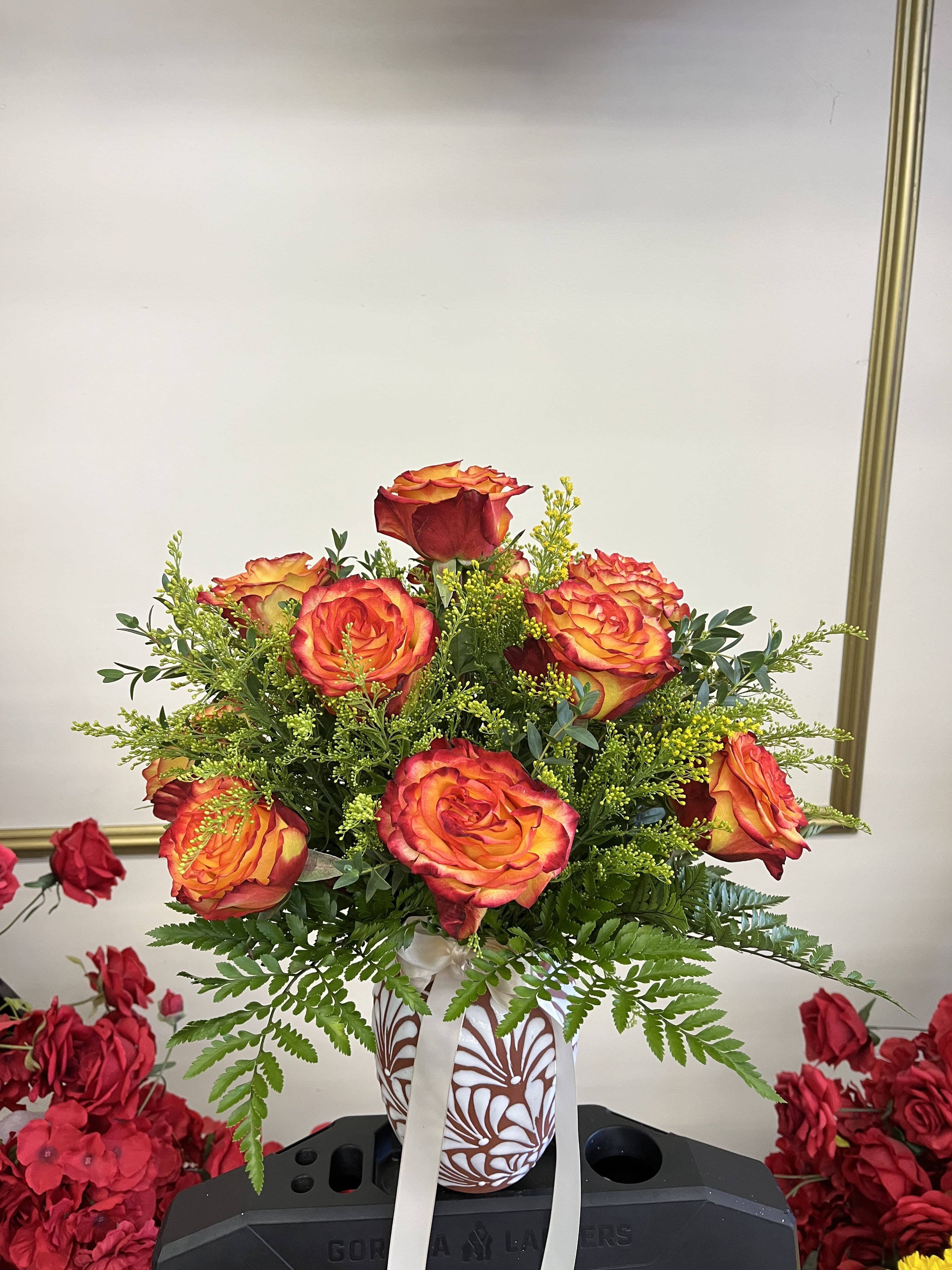 Orange-red roses in a patterned vase with a white ribbon