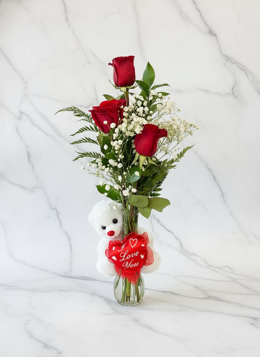 Three red roses in a glass vase with a teddy bear and heart tag