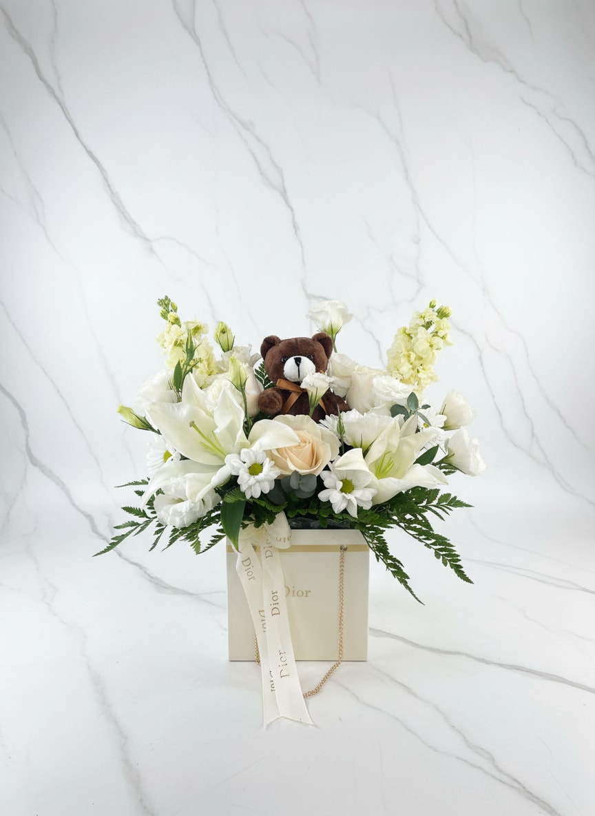 White floral arrangement with a small teddy bear in a Dior gift box