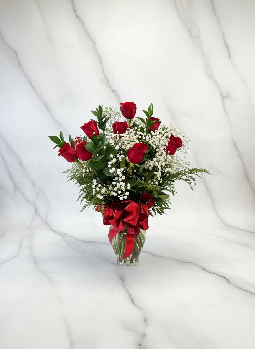 Red roses in a glass vase with baby's breath and a red ribbon
