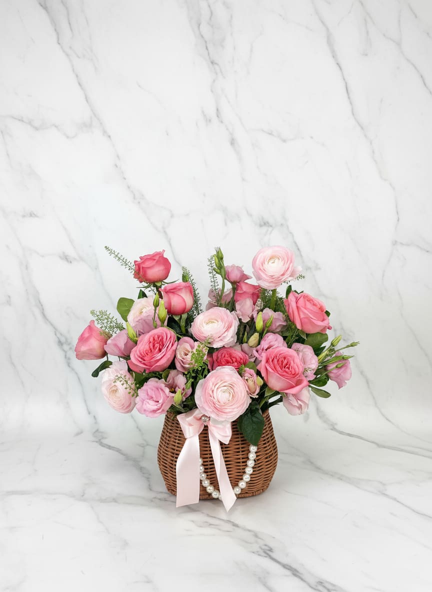 Pink rose and ranunculus arrangement in a wicker basket with a ribbon