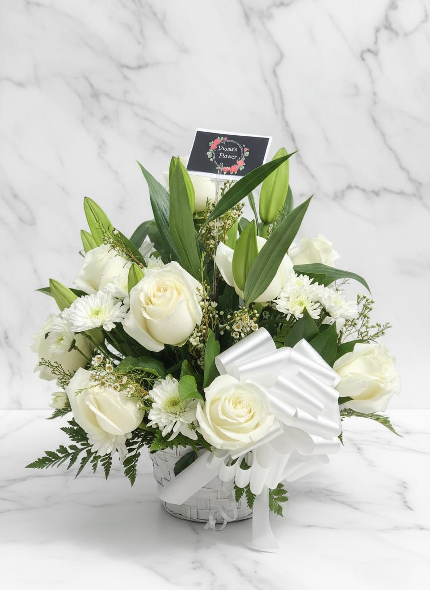 White roses and lilies arranged in a basket with a white ribbon