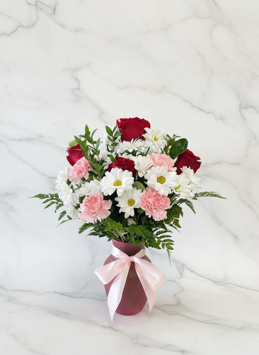 Bouquet of red roses, white daisies, and pink carnations in a pink vase