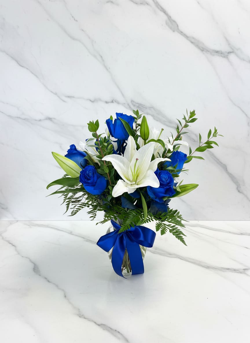 Blue roses and white lilies in a glass vase with a blue ribbon