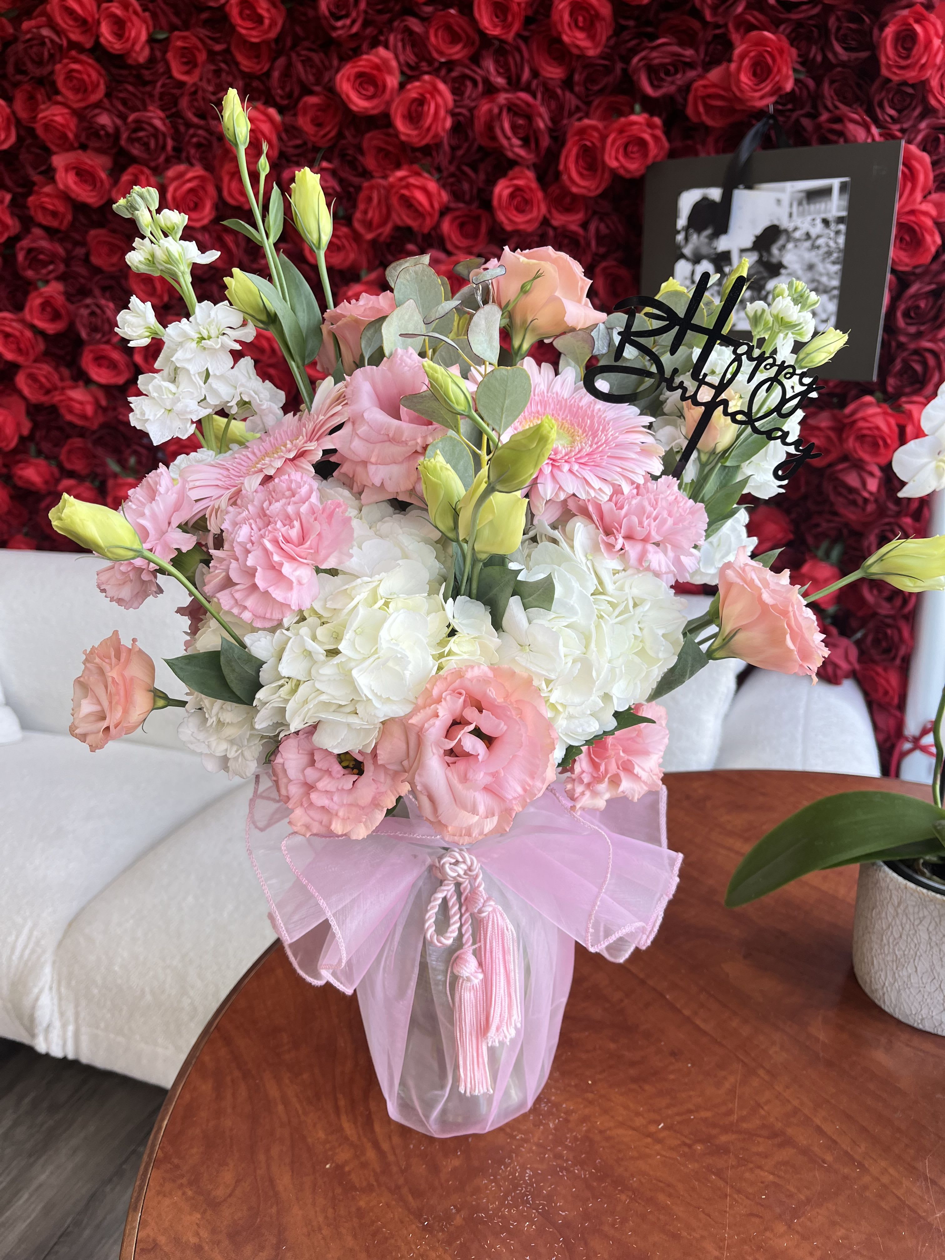 Pink and white bouquet in a clear vase with a birthday topper